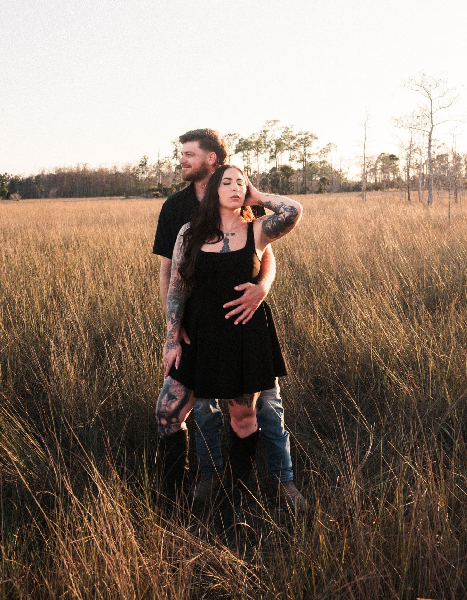 Playful couple dances and laughs together in tall grass during sunset.