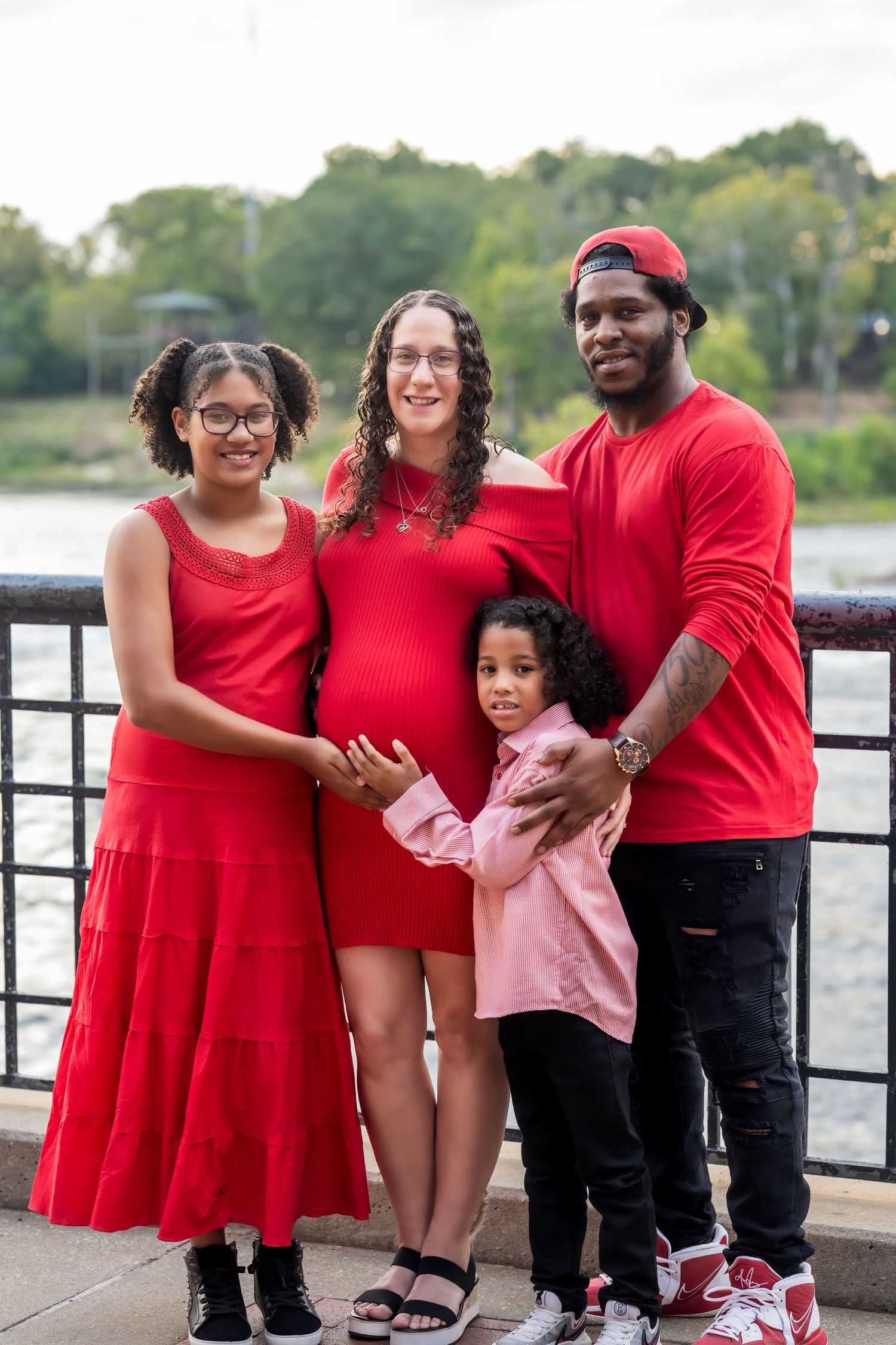 Family wearing coordinated red outfits poses together on rocky waterfront during outdoor photoshoot.