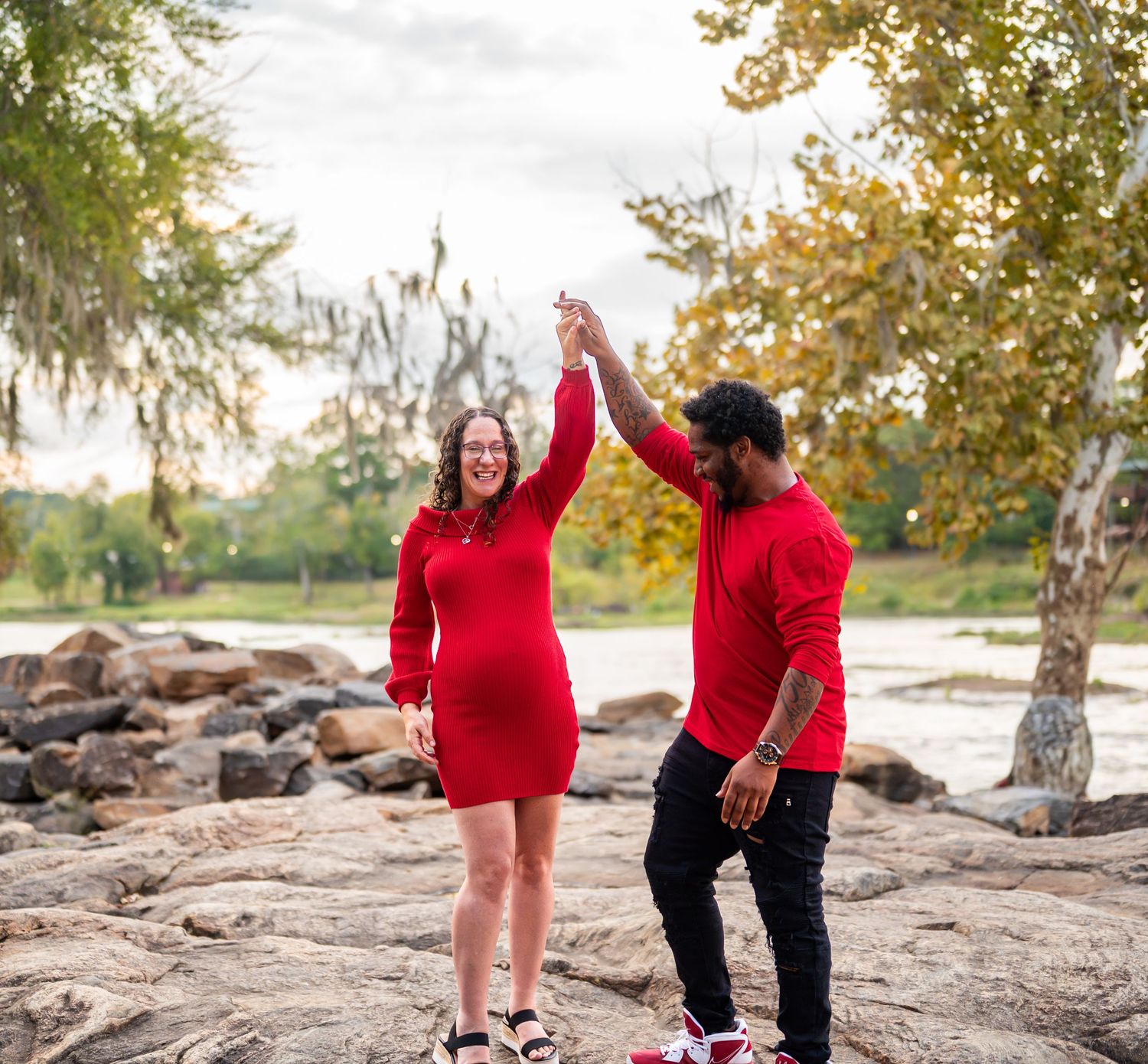 A couple wearing matching red outfits shares playful moments on a rocky landscape during autumn.