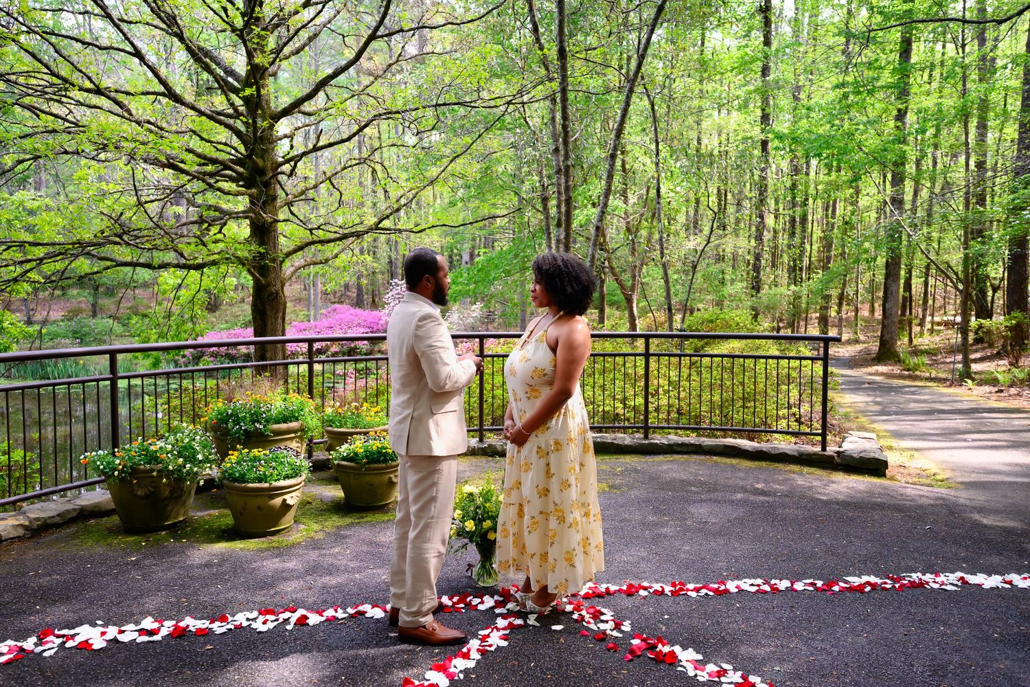 Couple standing together on a petal-decorated patio surrounded by blooming azaleas and tall trees.