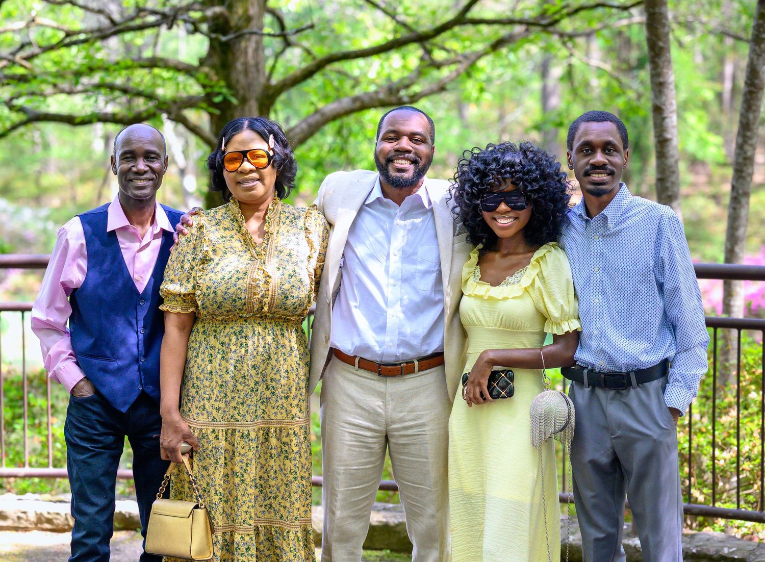 A joyful group of five people posing together outdoors in a lush green garden setting.