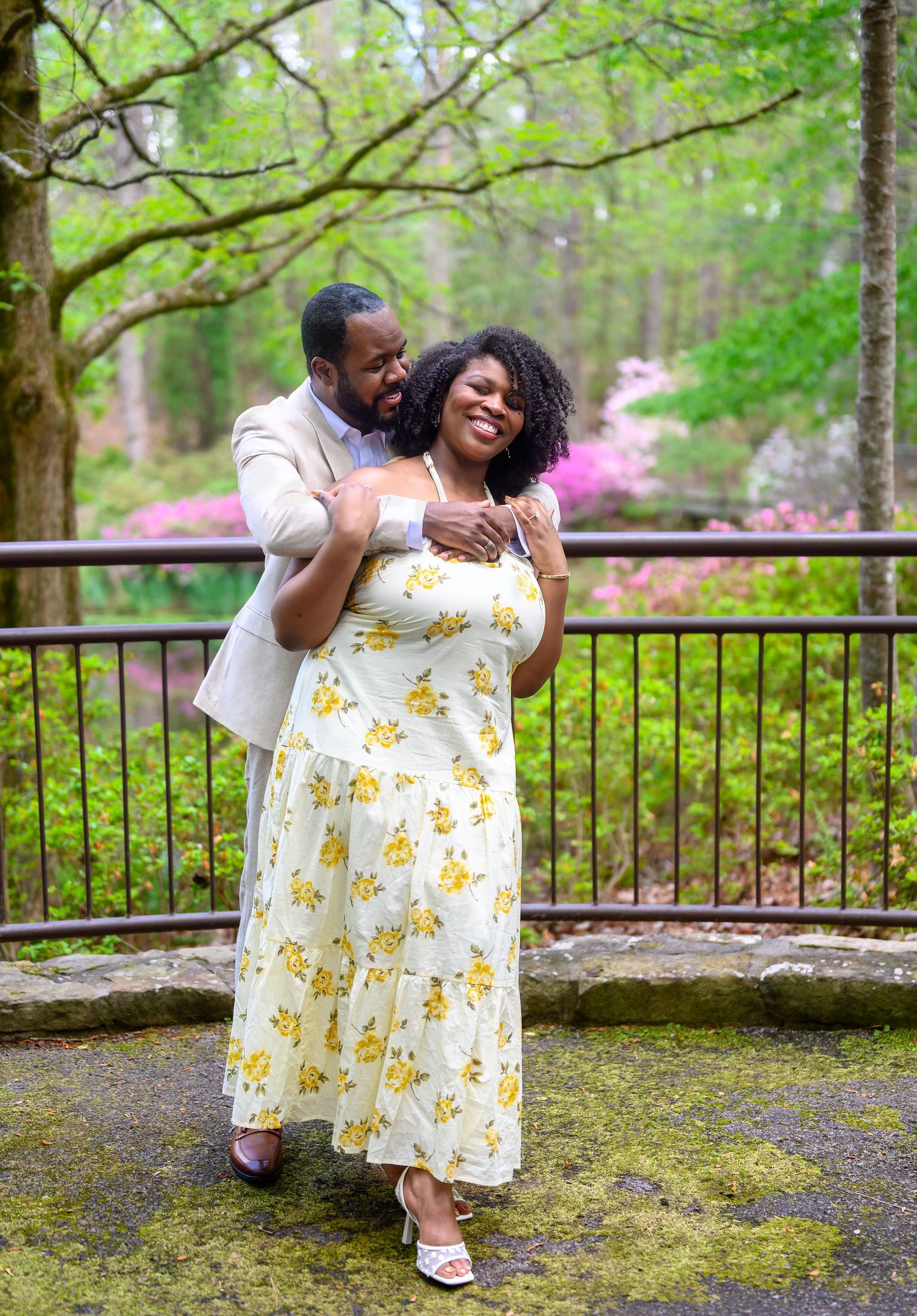 Couple sharing a joyful embrace on a mossy bridge with colorful azaleas behind them.