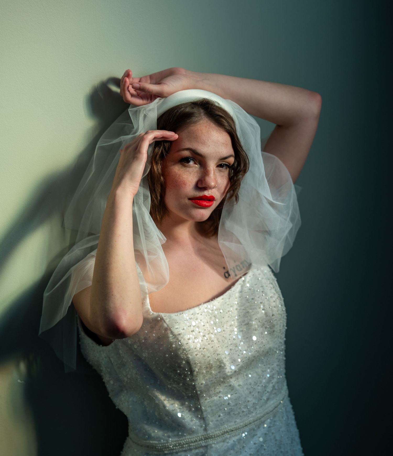 A bride in a sparkling white gown and veil poses elegantly against a moody dark backdrop with dramatic lighting.