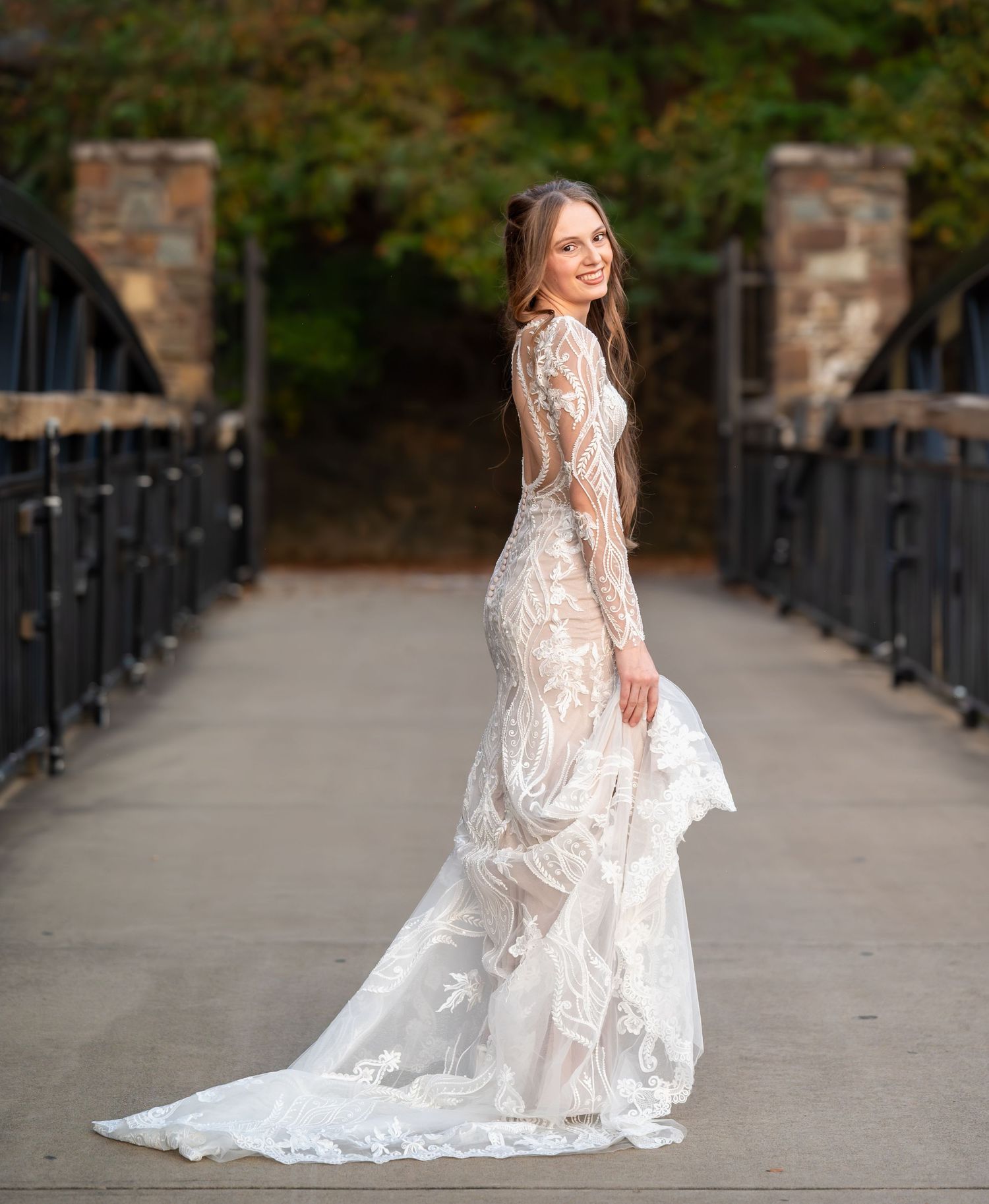 Elegant bridal photos on a stone bridge walkway showcasing the flowing train of a lace wedding gown.