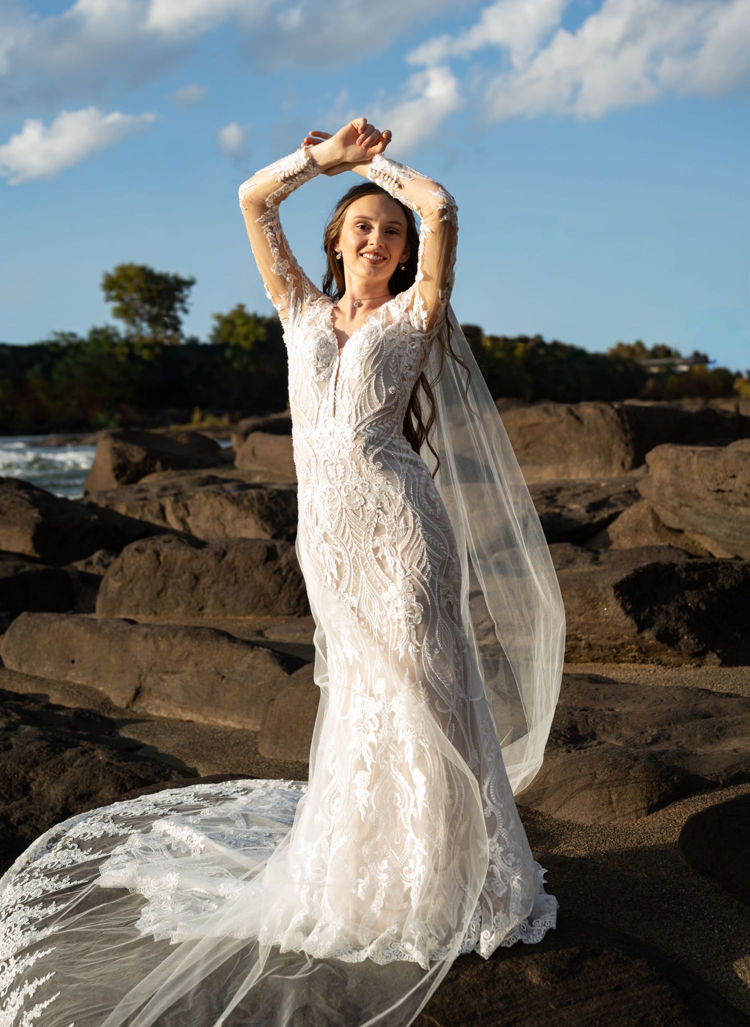 An ethereal bridal portrait features a delicate lace gown with flowing veil against dramatic rocky landscape.