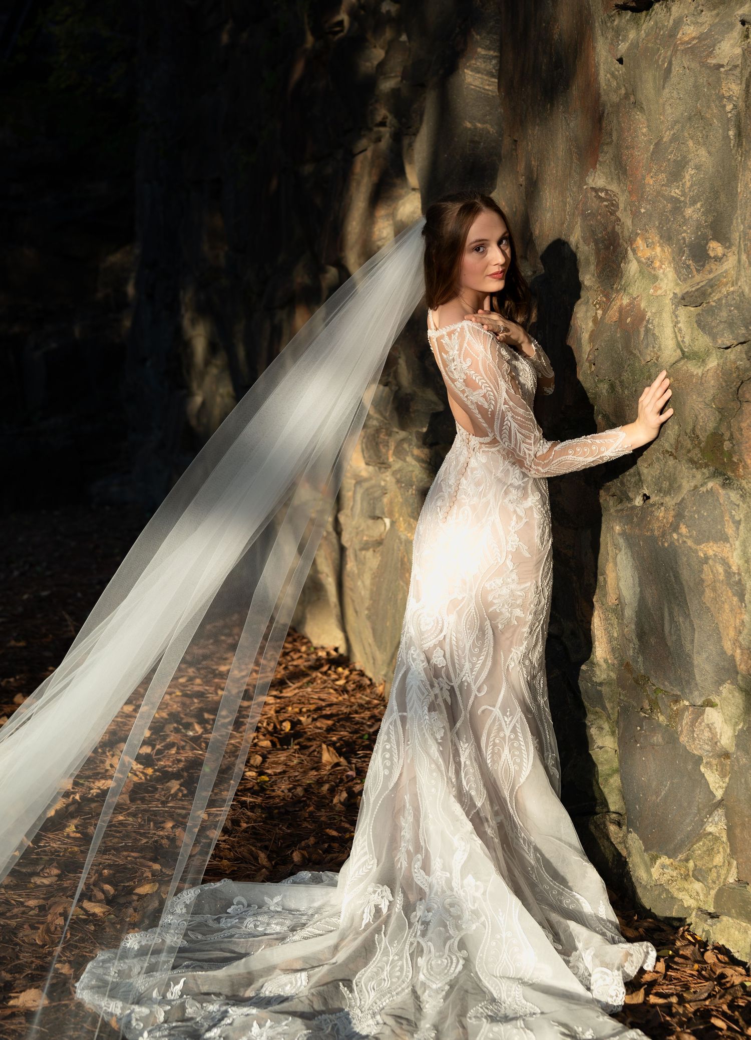 Artistic bridal portraits against textured stone walls with dramatic lighting and fallen autumn leaves.