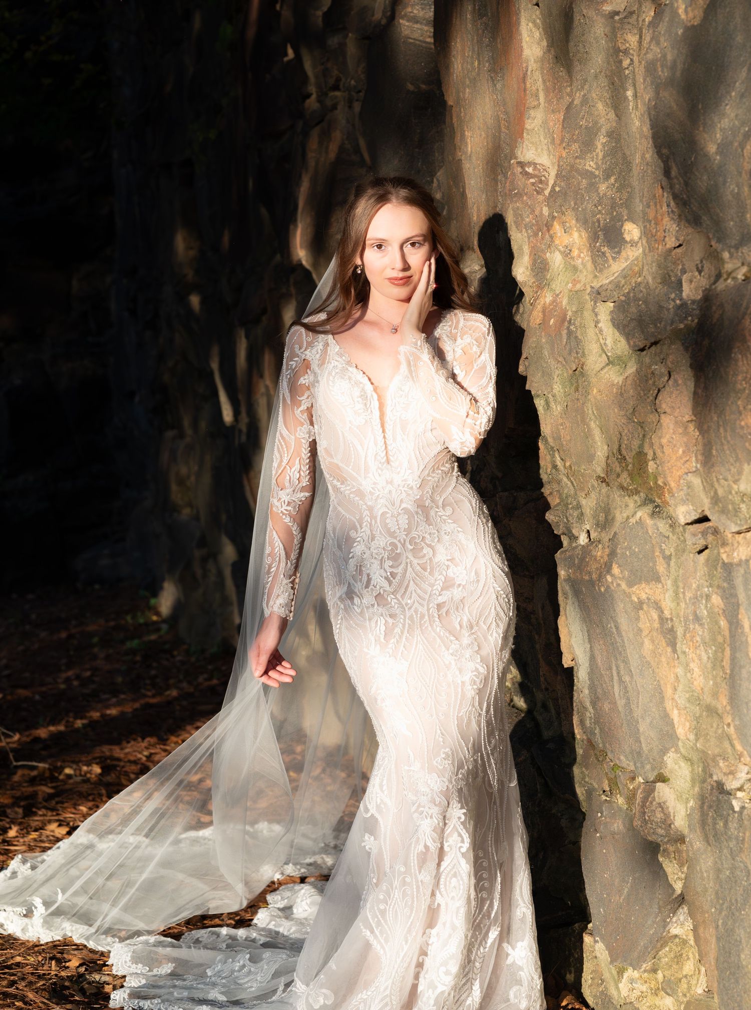 Dramatic bridal portrait against textured stone wall with flowing veil and lace details.