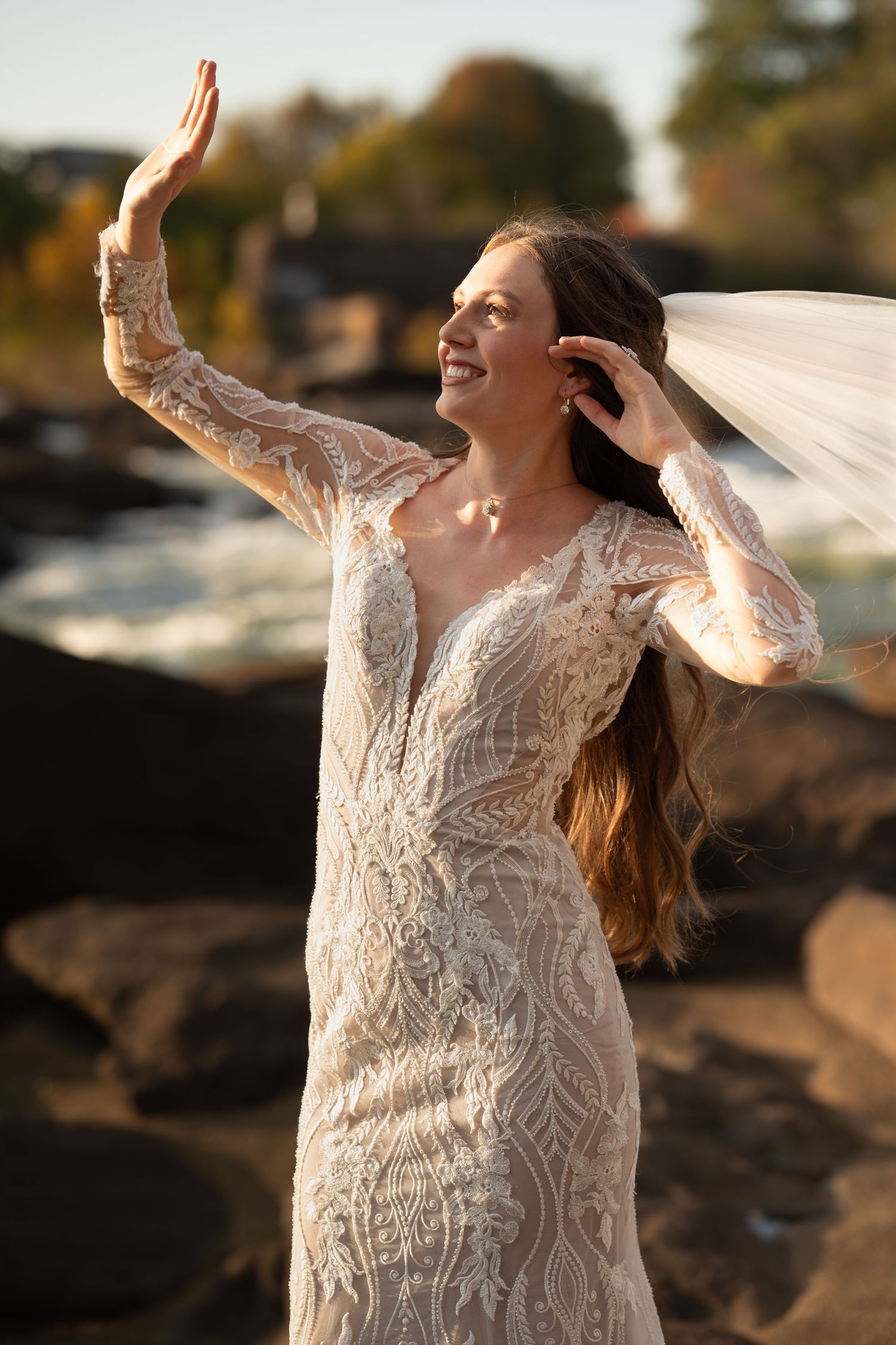Joyful bridal portraits with flowing veil and lace dress against sunset lighting.