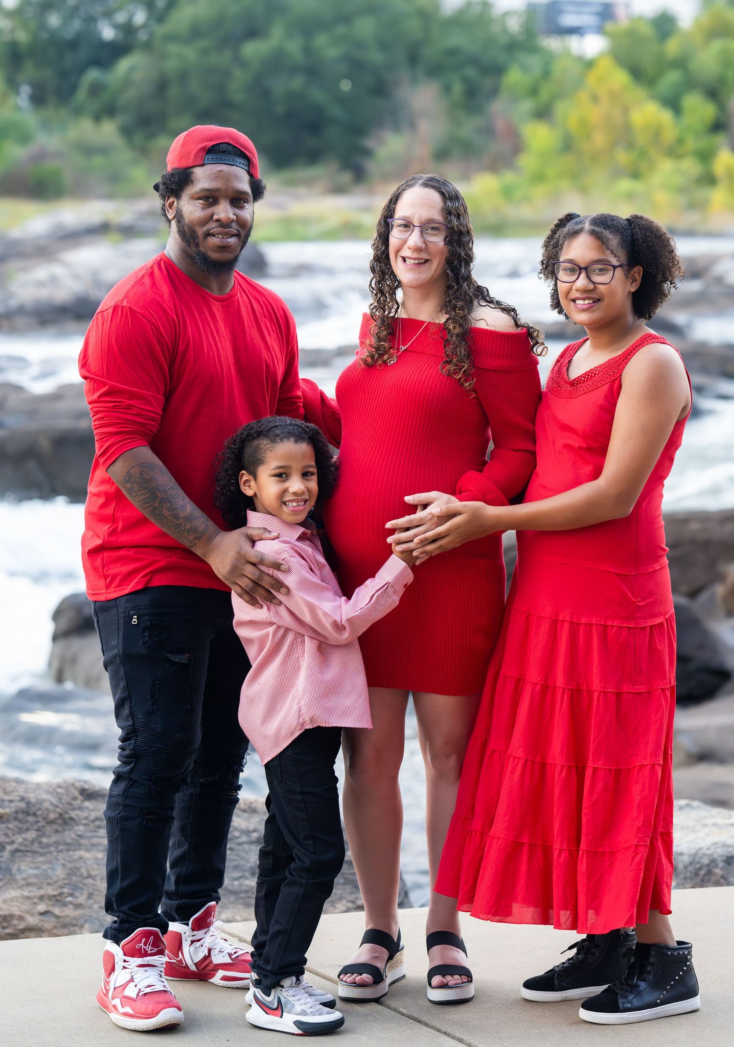 Group in matching red outfits smiles and embraces while standing on rocky shoreline.