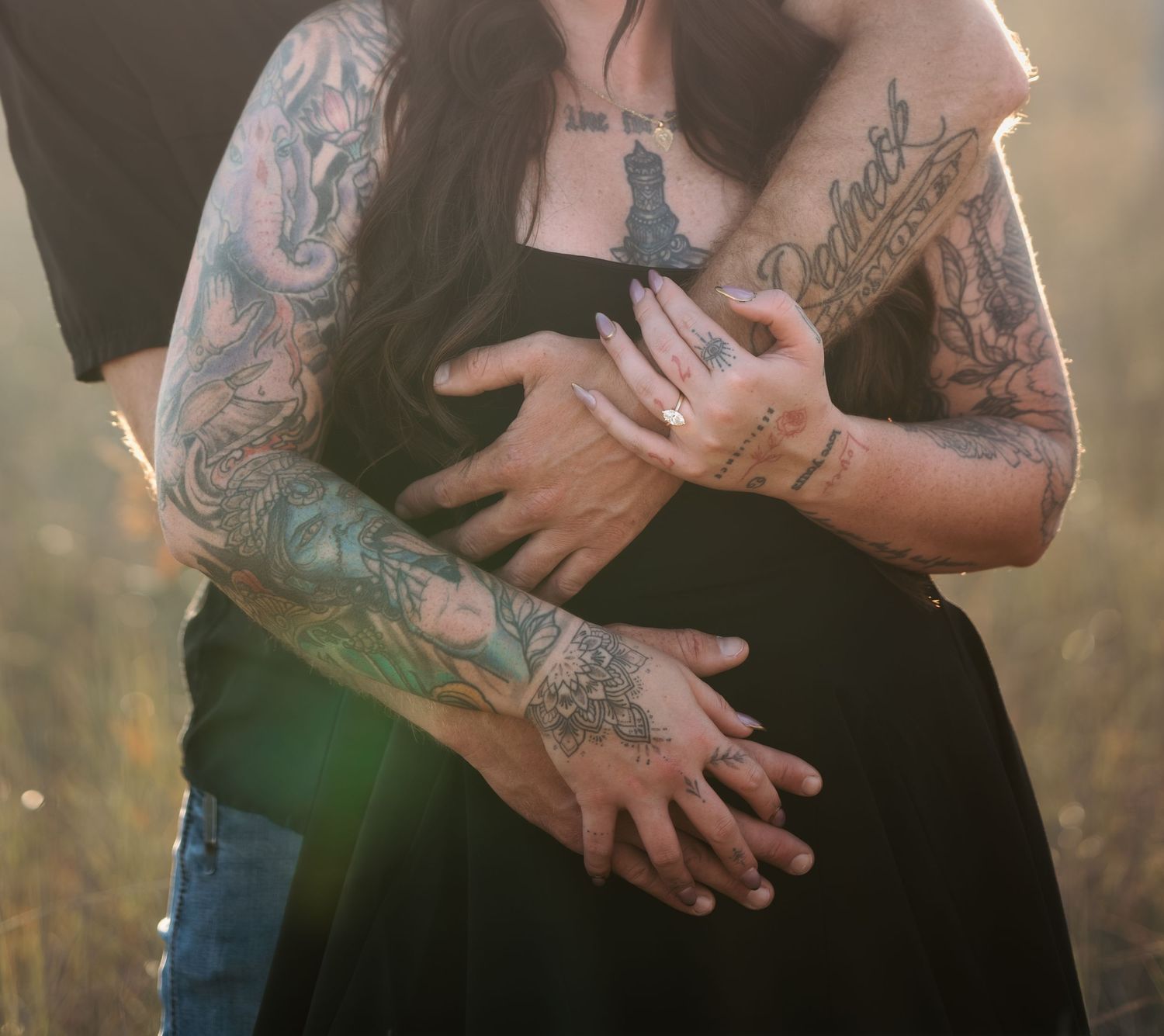 Tattooed arms embrace in warm sunlight during an intimate outdoor photoshoot.