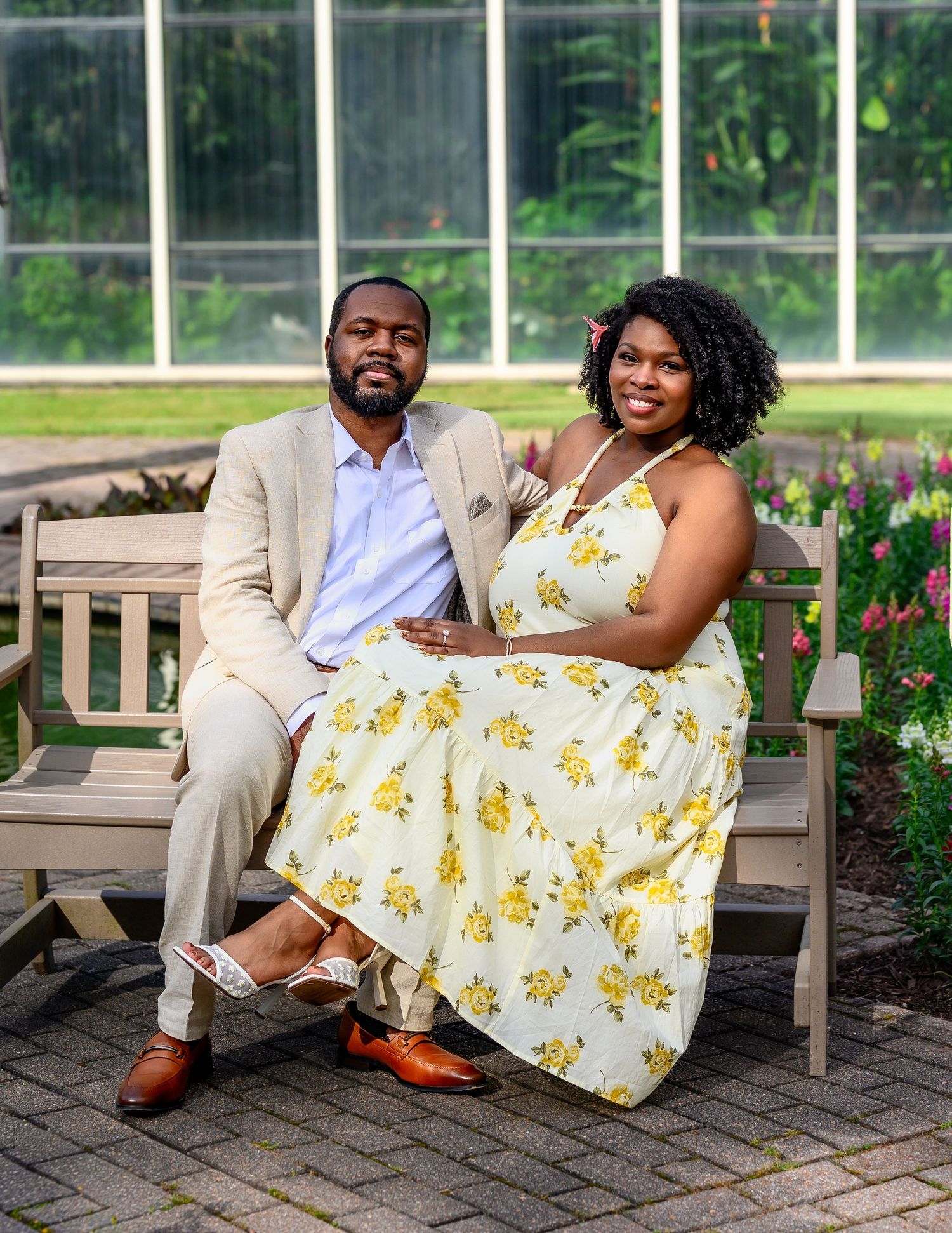 Couple posing on garden bench with greenhouse backdrop in wedding attire.