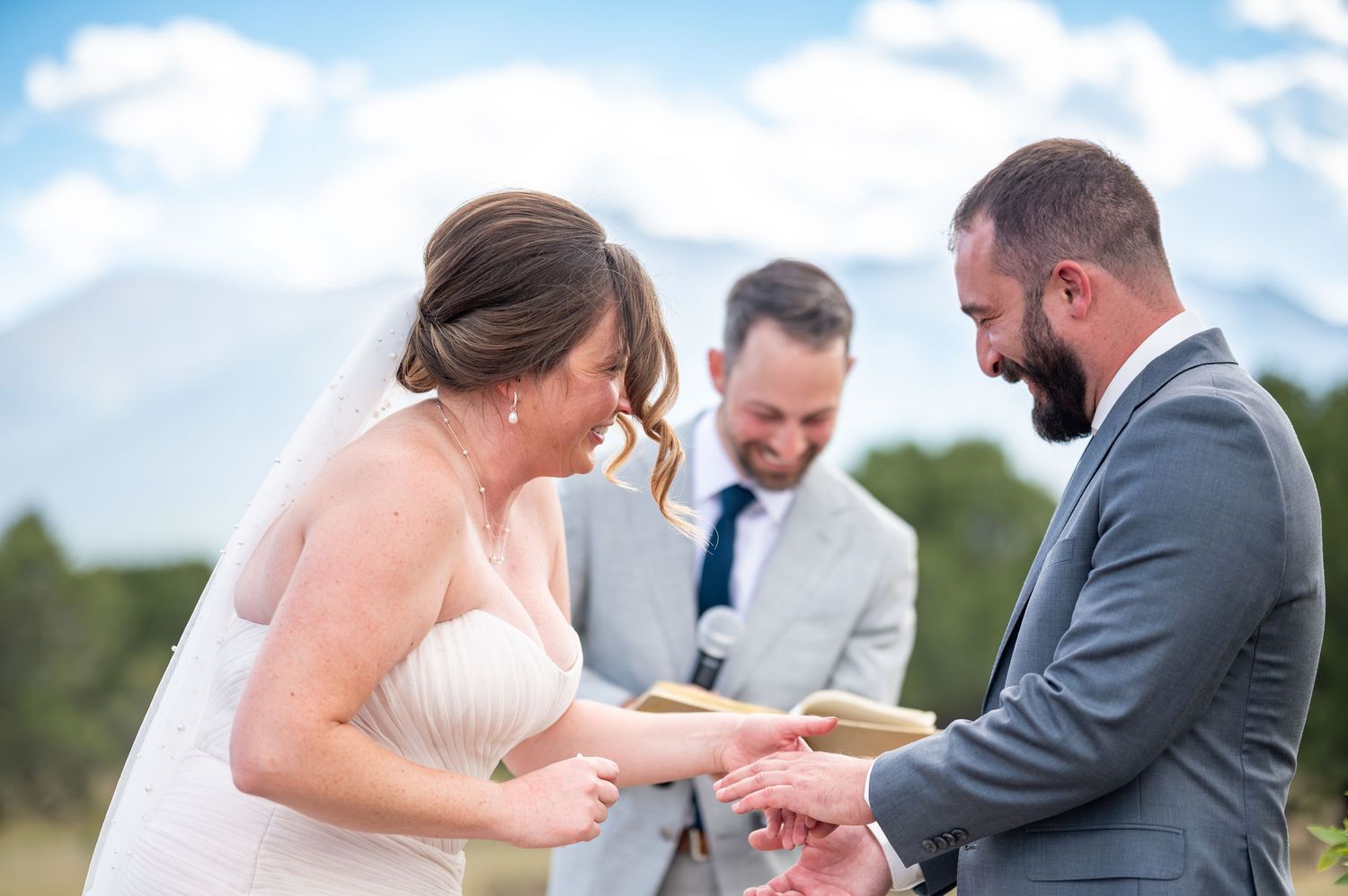 Wedding ceremony exchange beneath blue skies with mountain range backdrop.