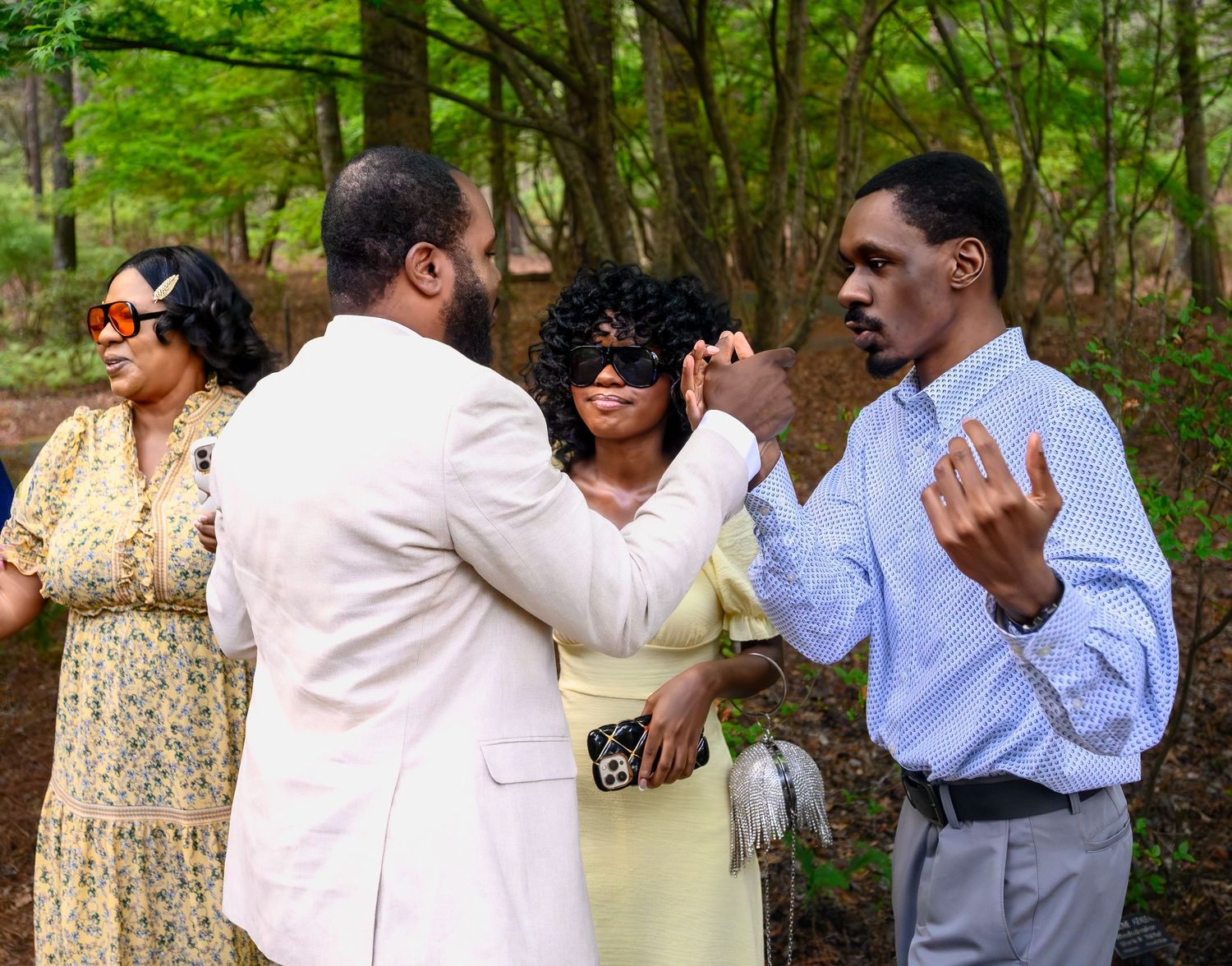 Family and friends celebrating joyfully outdoors in wooded setting after a surprise marriage proposal.