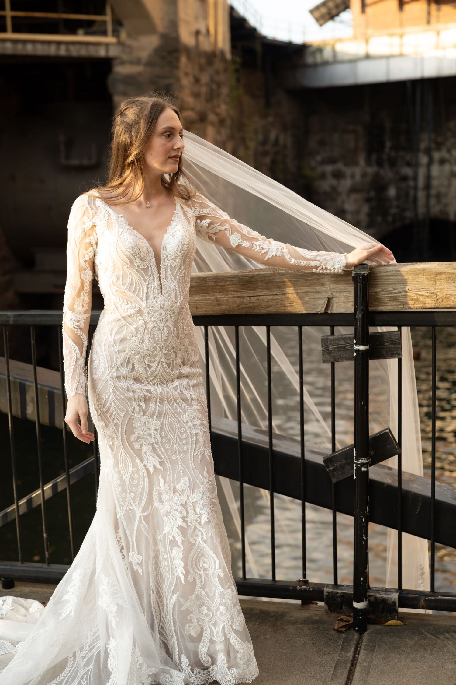 A lace wedding dress with long sleeves photographed against metal railings and stone architecture.