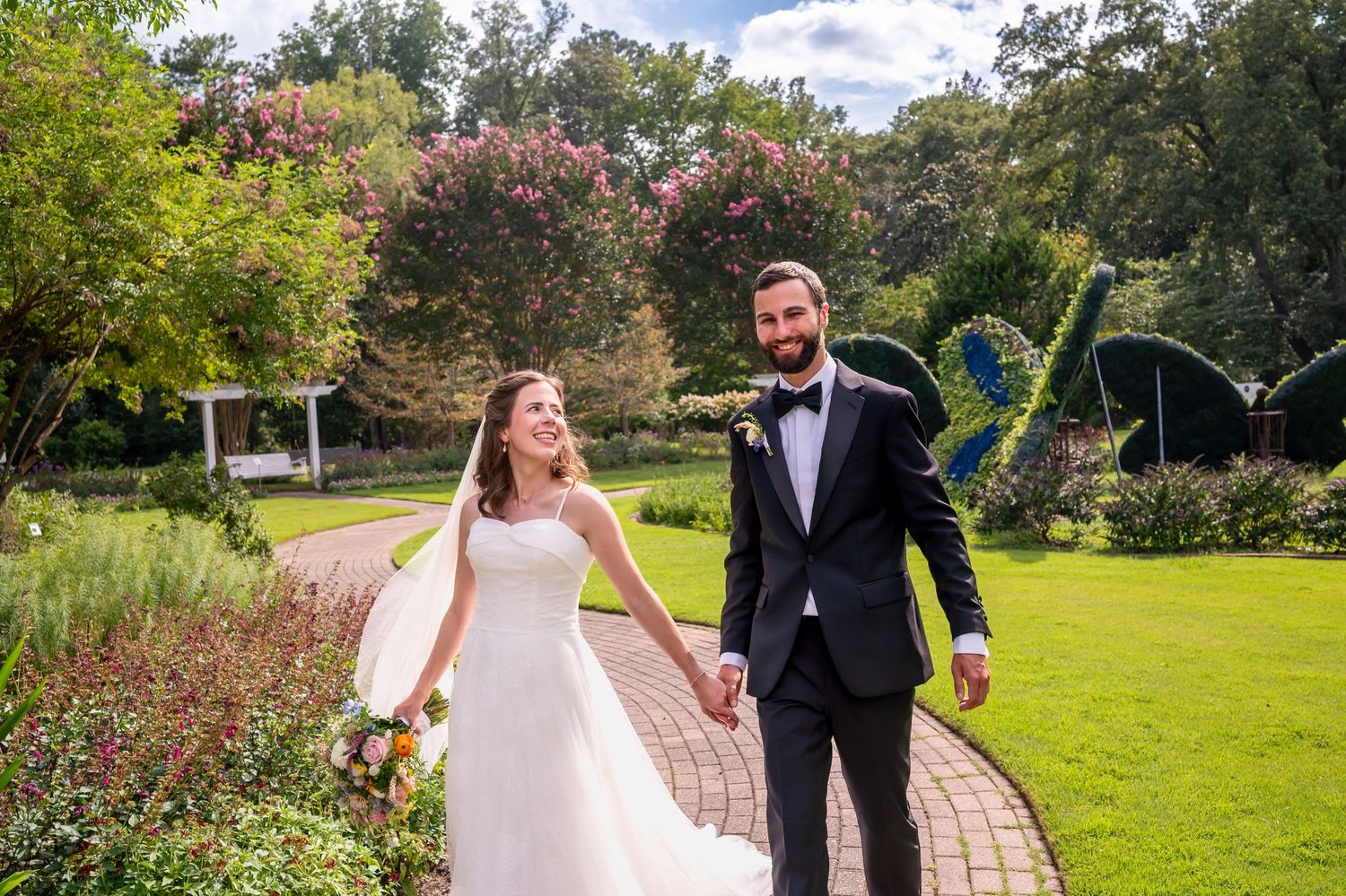 A couple in wedding attire walks together through a scenic garden path on their special day.