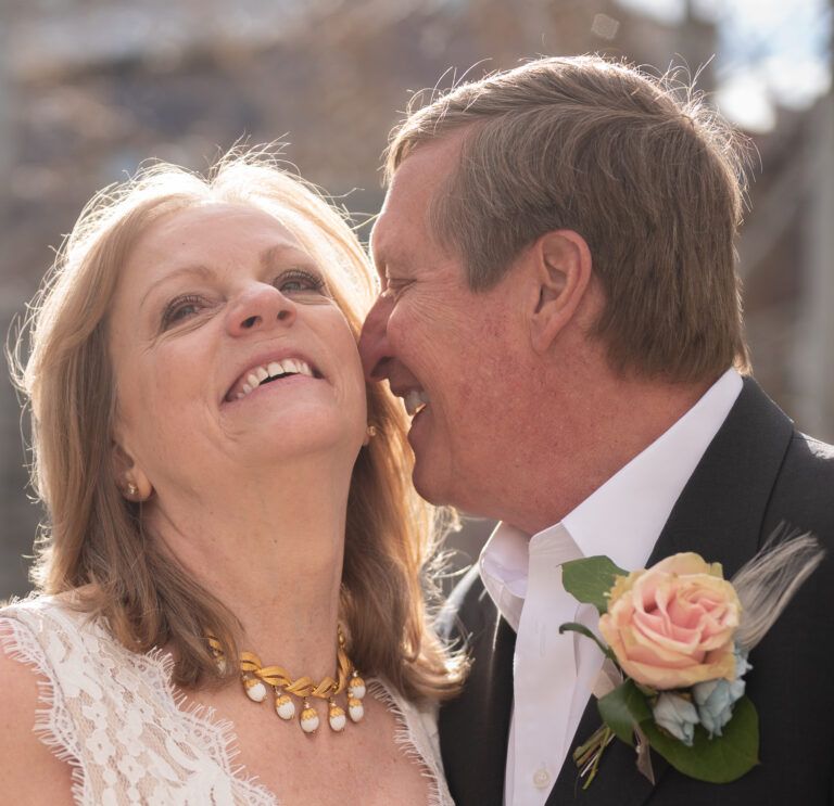 Candid moment of newlyweds sharing joyful laughter with peach rose boutonniere.
