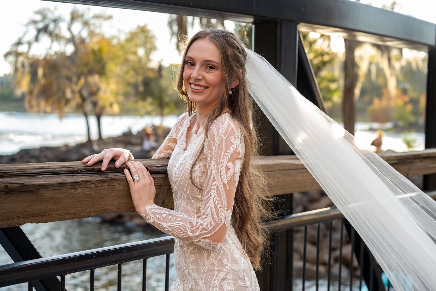 Bridal portraits on wooden deck with scenic water view and autumn foliage.