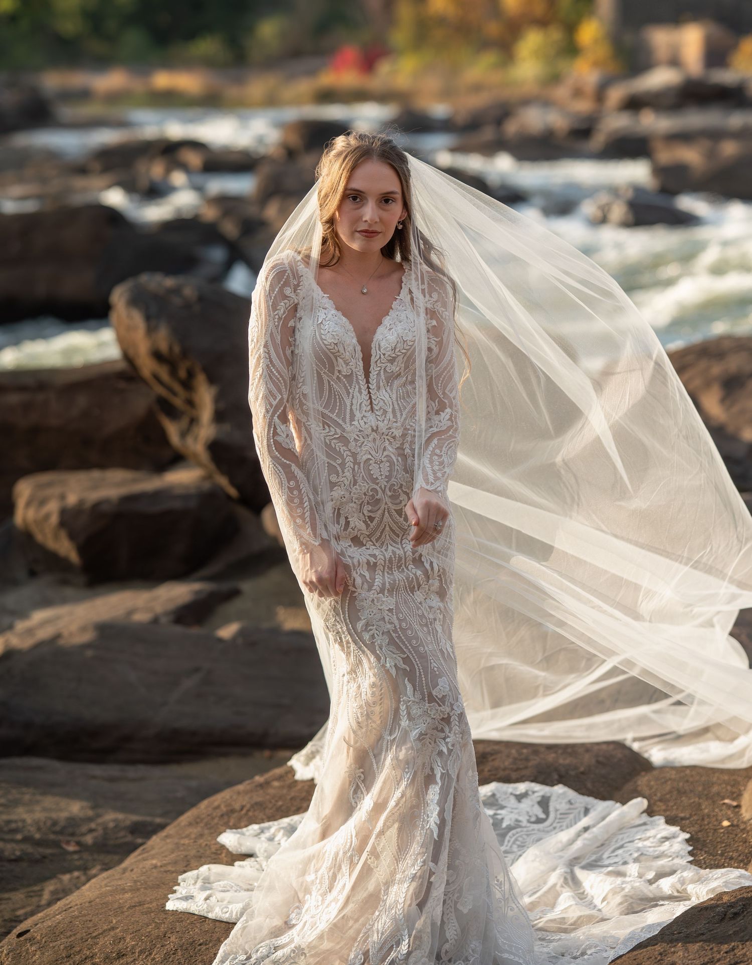 Wedding dress with intricate lace details and long train photographed on coastal rocks.