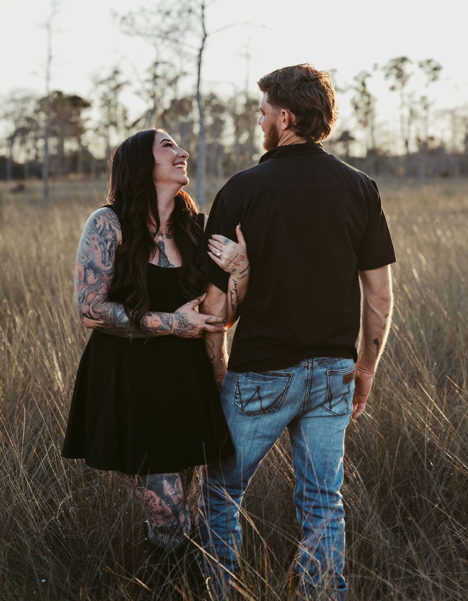 A couple shares an intimate moment in a sunlit field of tall grass at sunset.