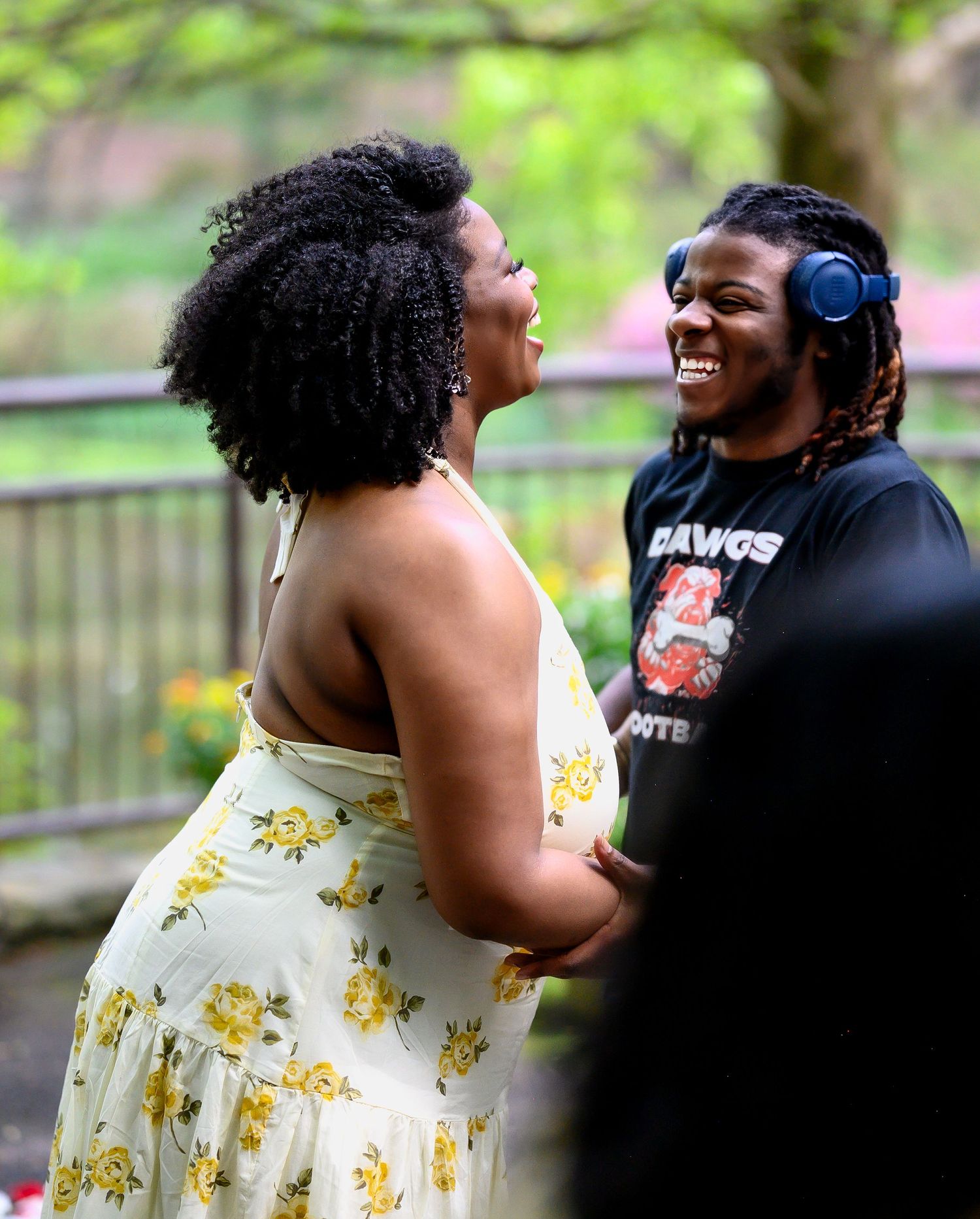 Joyful couple laughing together outdoors during engagement celebration, woman in yellow floral dress.