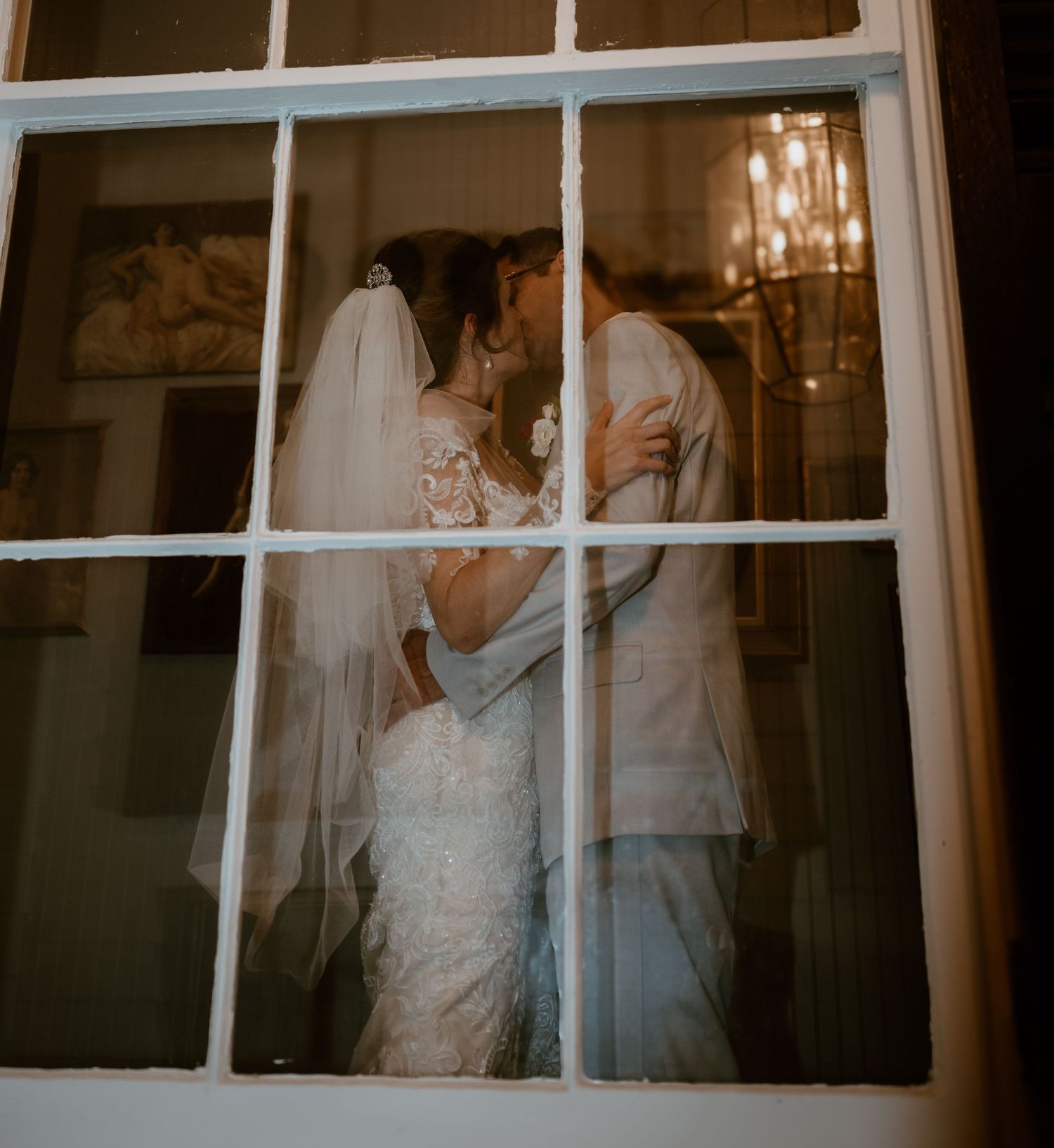 Intimate wedding couple moment captured through window panes in warm lighting.