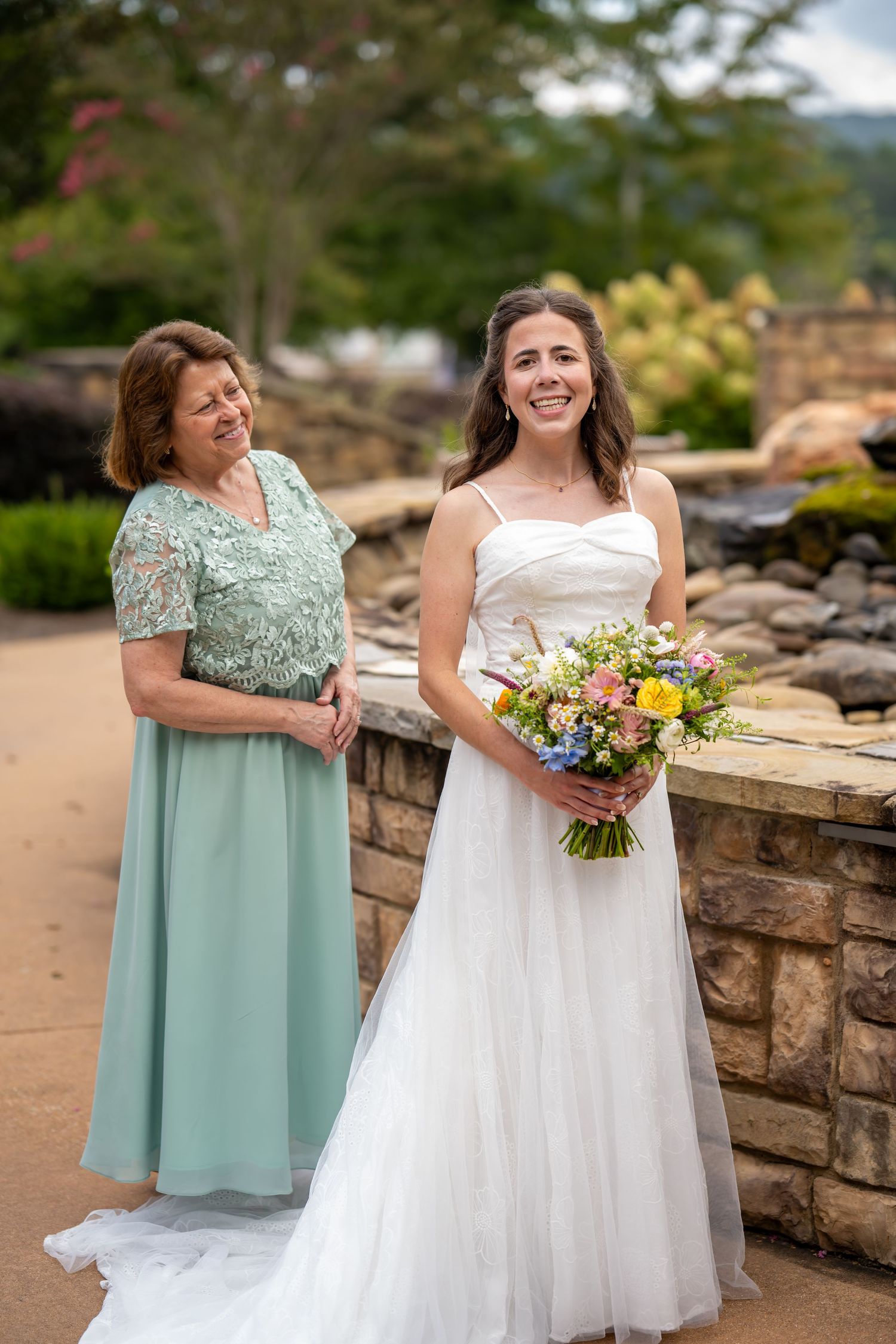 Two people in mint green and white dresses share a joyful moment together on a stone wall terrace.