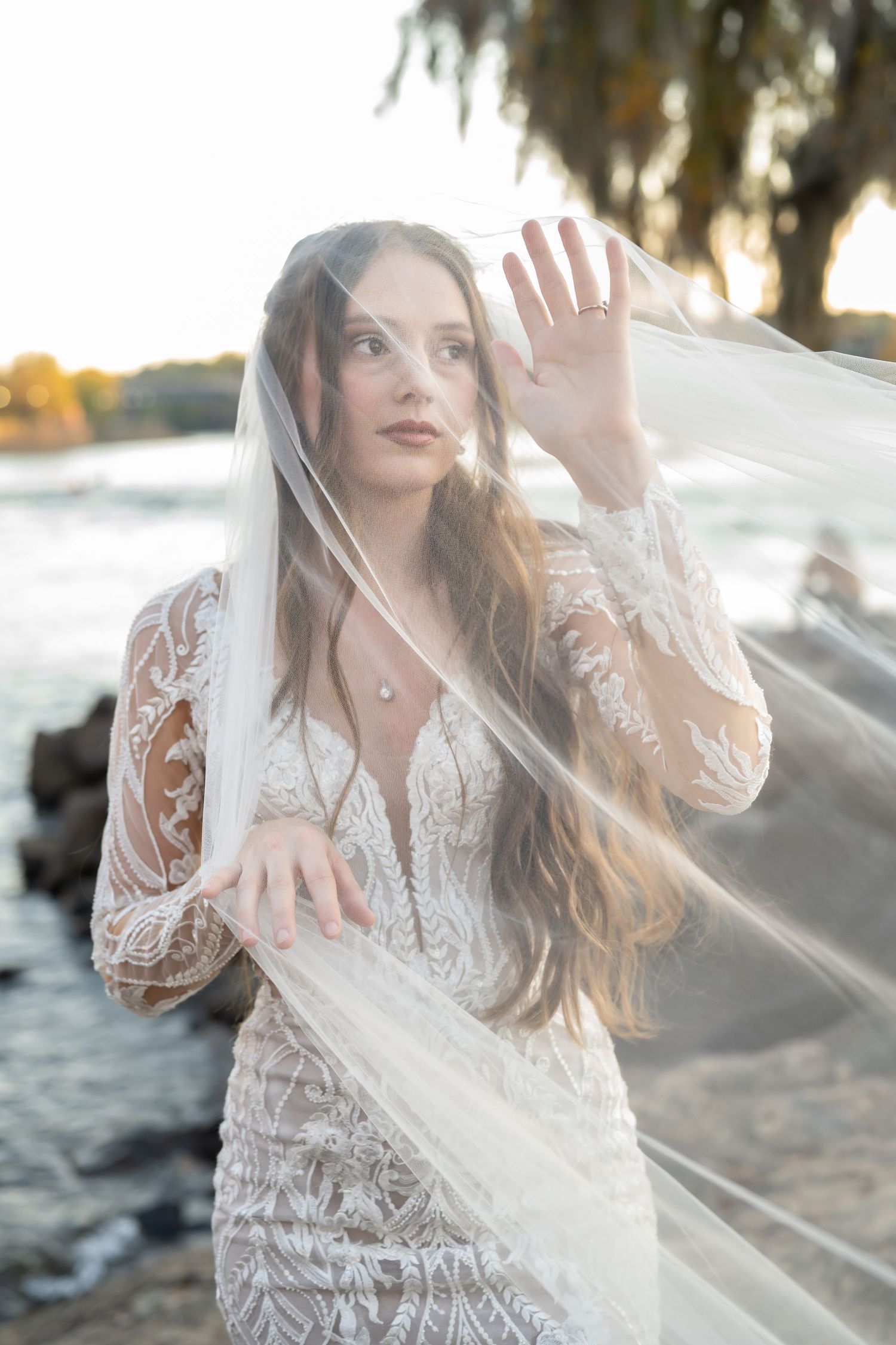 Sunlit bridal portrait with flowing veil and intricate lace dress details captured at golden hour.