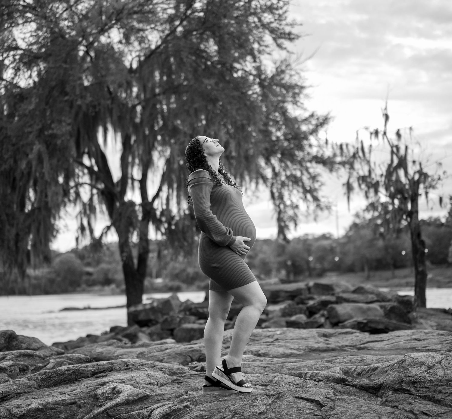 Silhouette of pregnant figure standing on rocks against a backdrop of Spanish moss hanging from trees.
