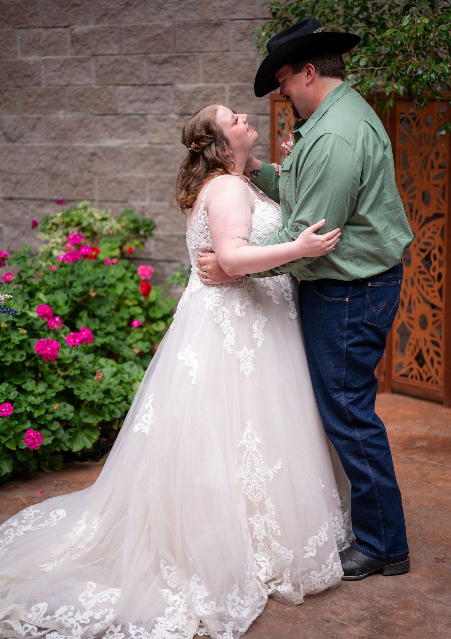 Wedding couple shares intimate moment surrounded by blooming pink flowers and rustic decor.