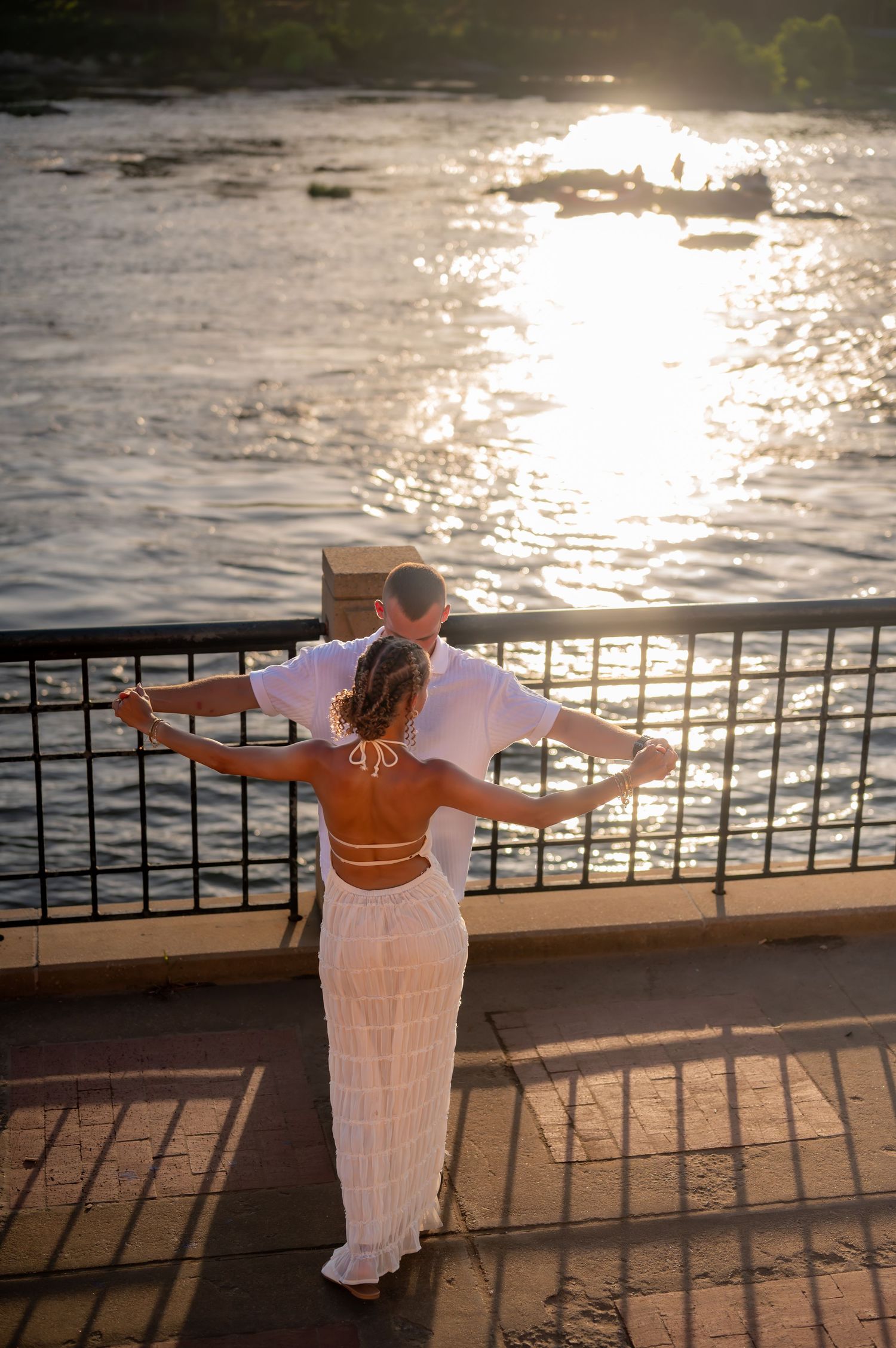 Figure in flowing white dress strikes graceful poses against sunset-lit waterfront railing.