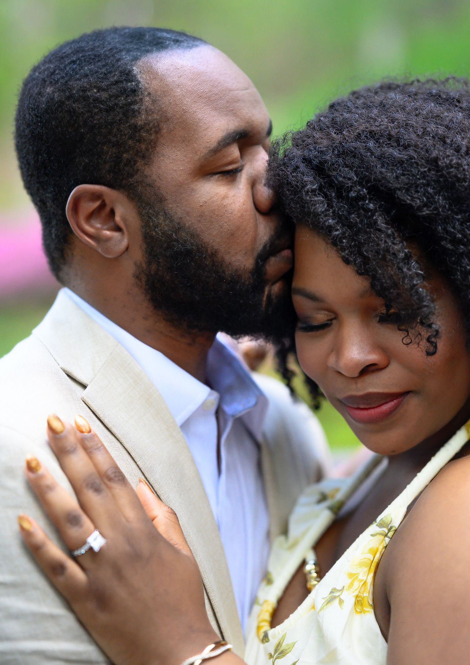 Close-up of man kissing womans forehead while she displays her diamond engagement ring.