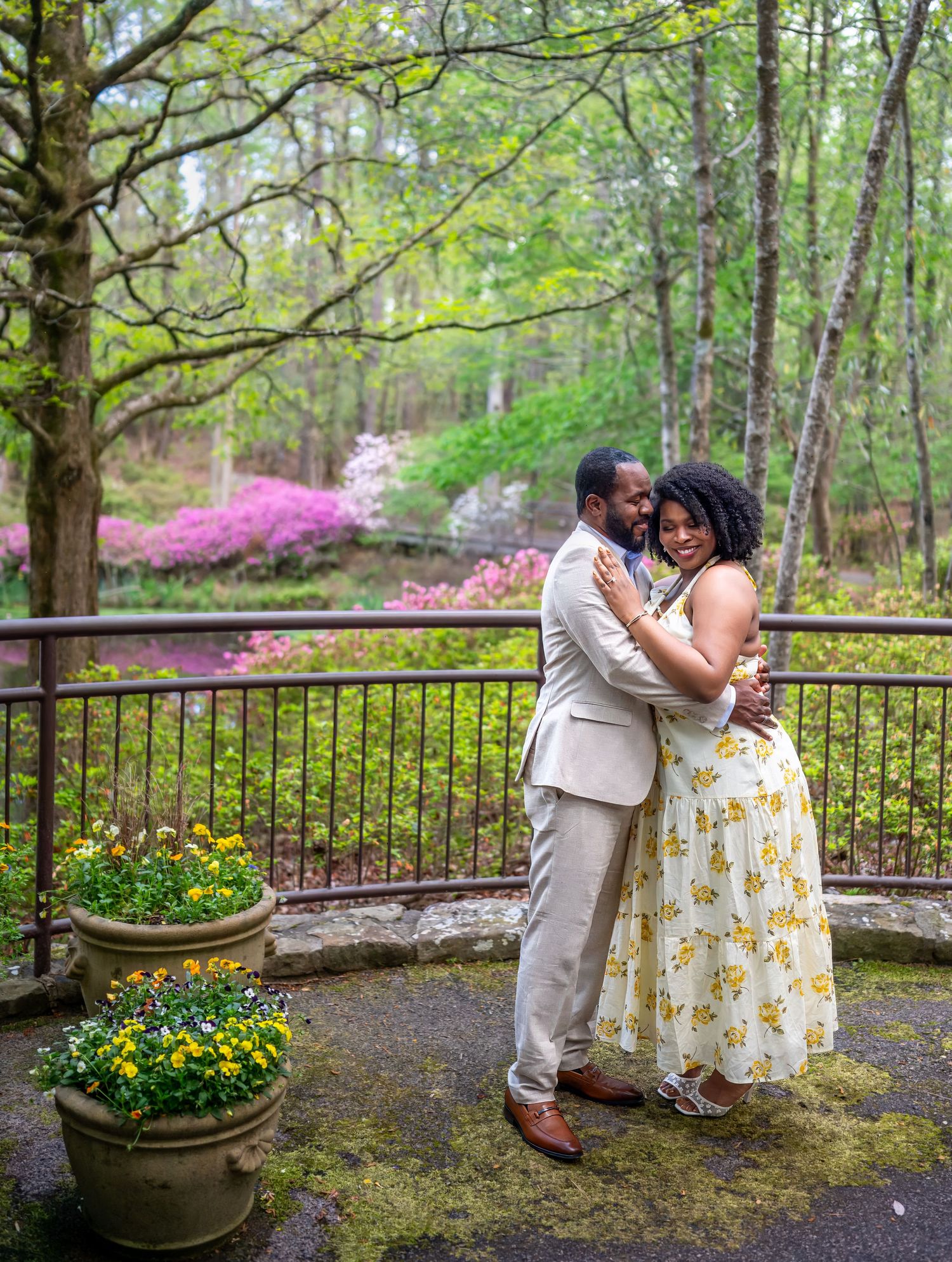 Couple embracing romantically on a garden terrace with colorful azaleas and lush greenery in the background.
