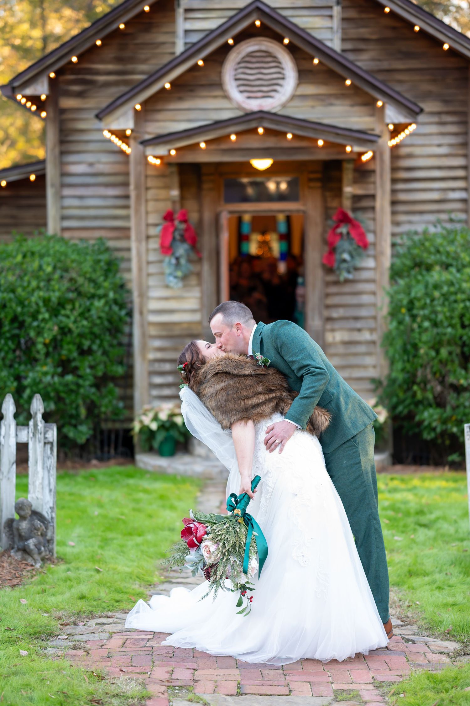 Romantic wedding dip kiss in front of rustic cabin decorated with holiday lights and wreaths.