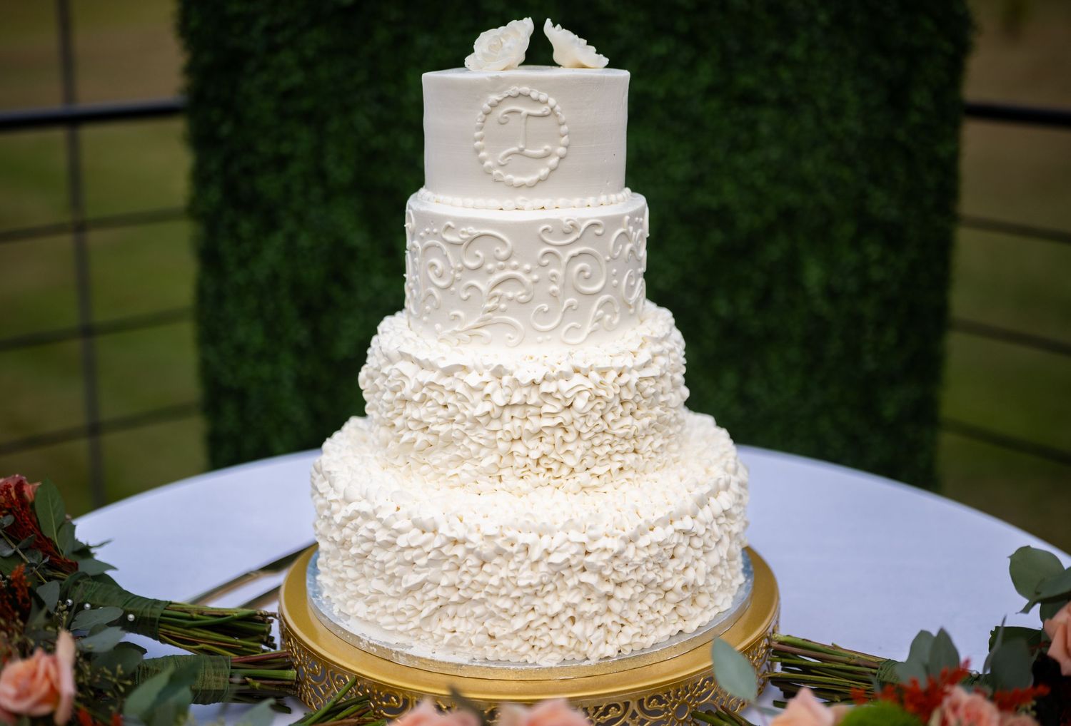 Elegant four-tier white wedding cake decorated with intricate lace patterns and floral designs on a gold stand.
