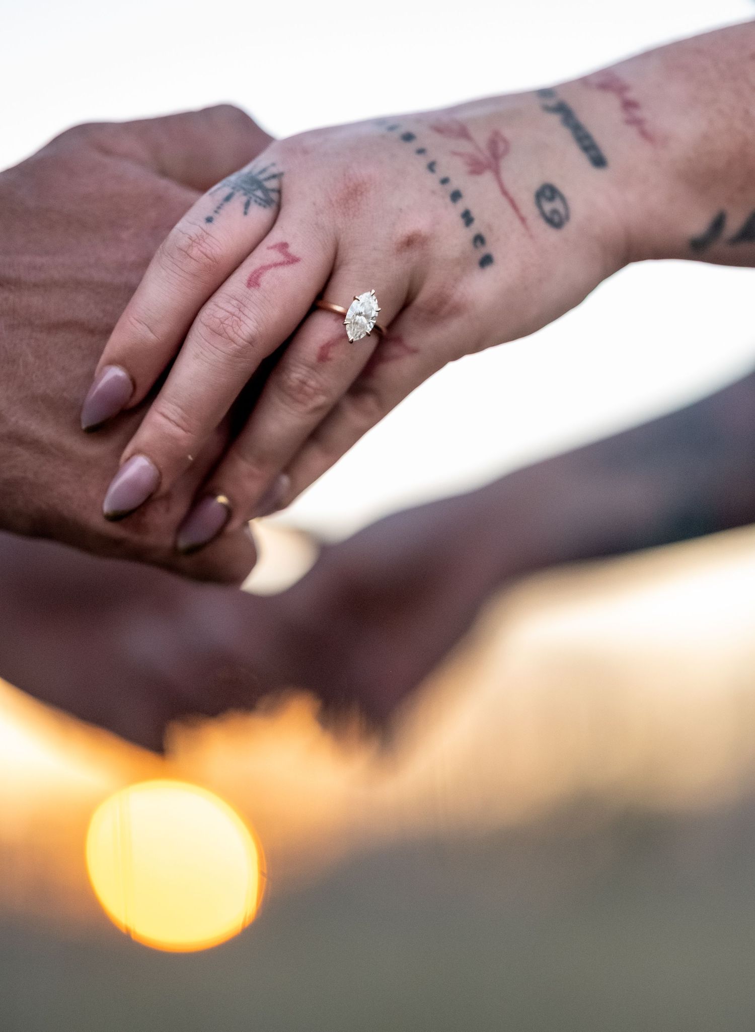 Close-up shots of hands with tattoos and an engagement ring against a sunset backdrop.
