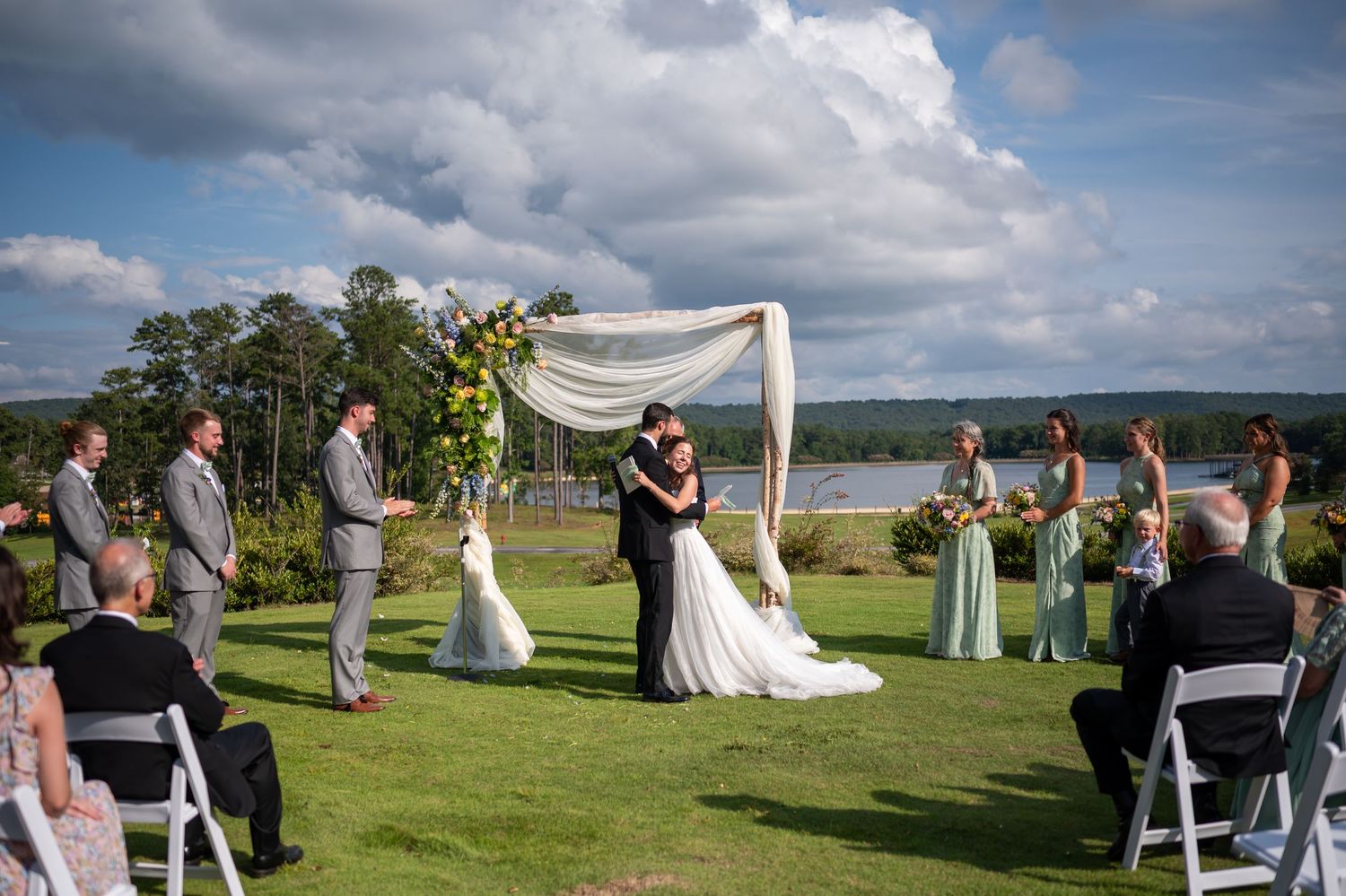 Outdoor wedding ceremony setup with white chairs and arch against rolling hills and cloudy skies.