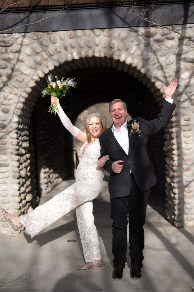 Excited senior couple who just eloped and are now husband and wife. They have their hands up in celebration. They're in front of a rock arch