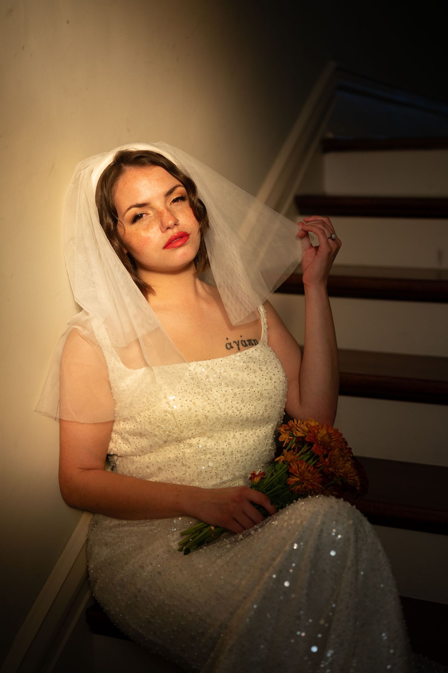 Bride in sparkly white wedding dress holds bouquet while posing dramatically in moody lighting and dark background.