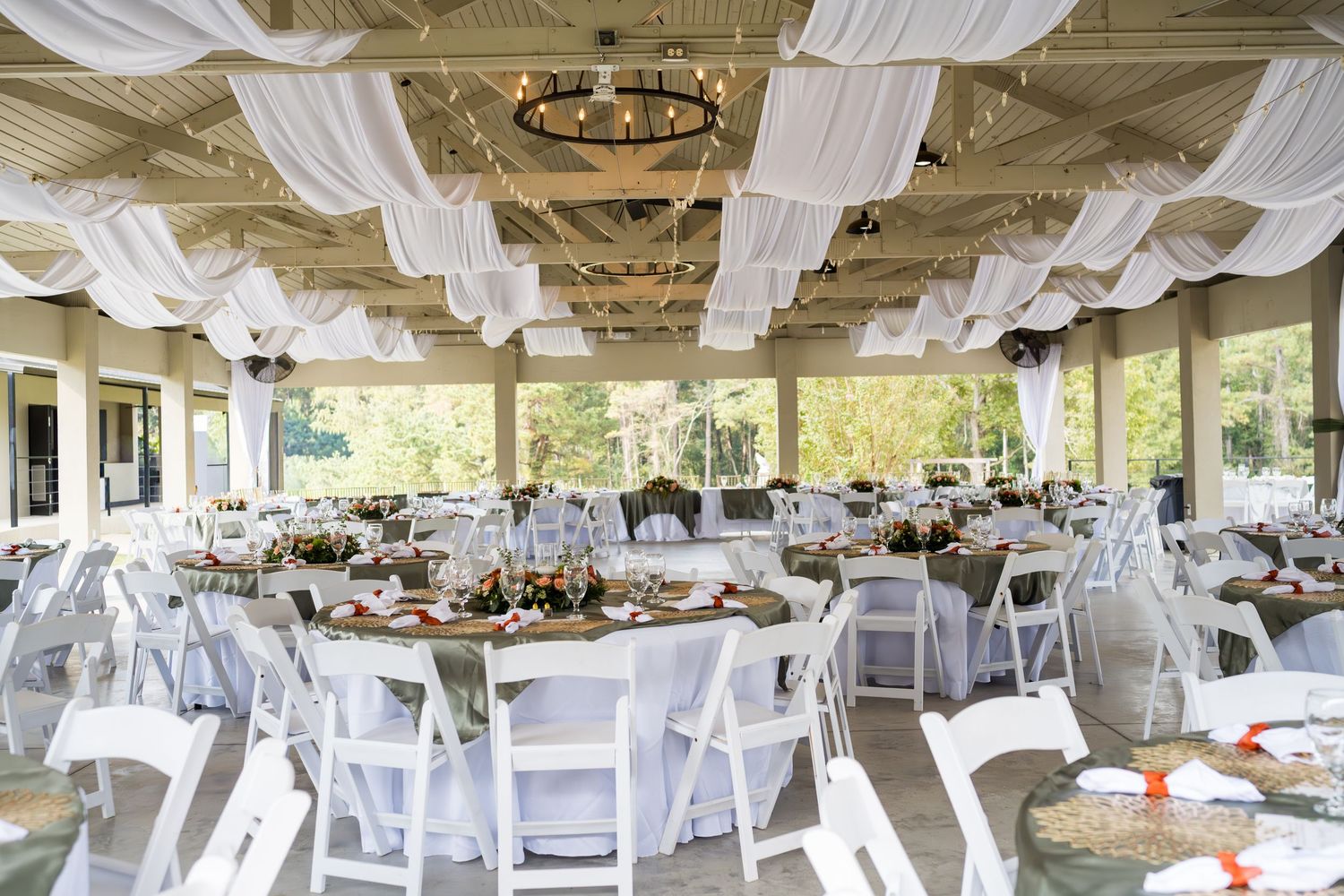 Elegant wedding reception venue with white draped ceiling, round tables, and folding chairs set up under a pavilion.
