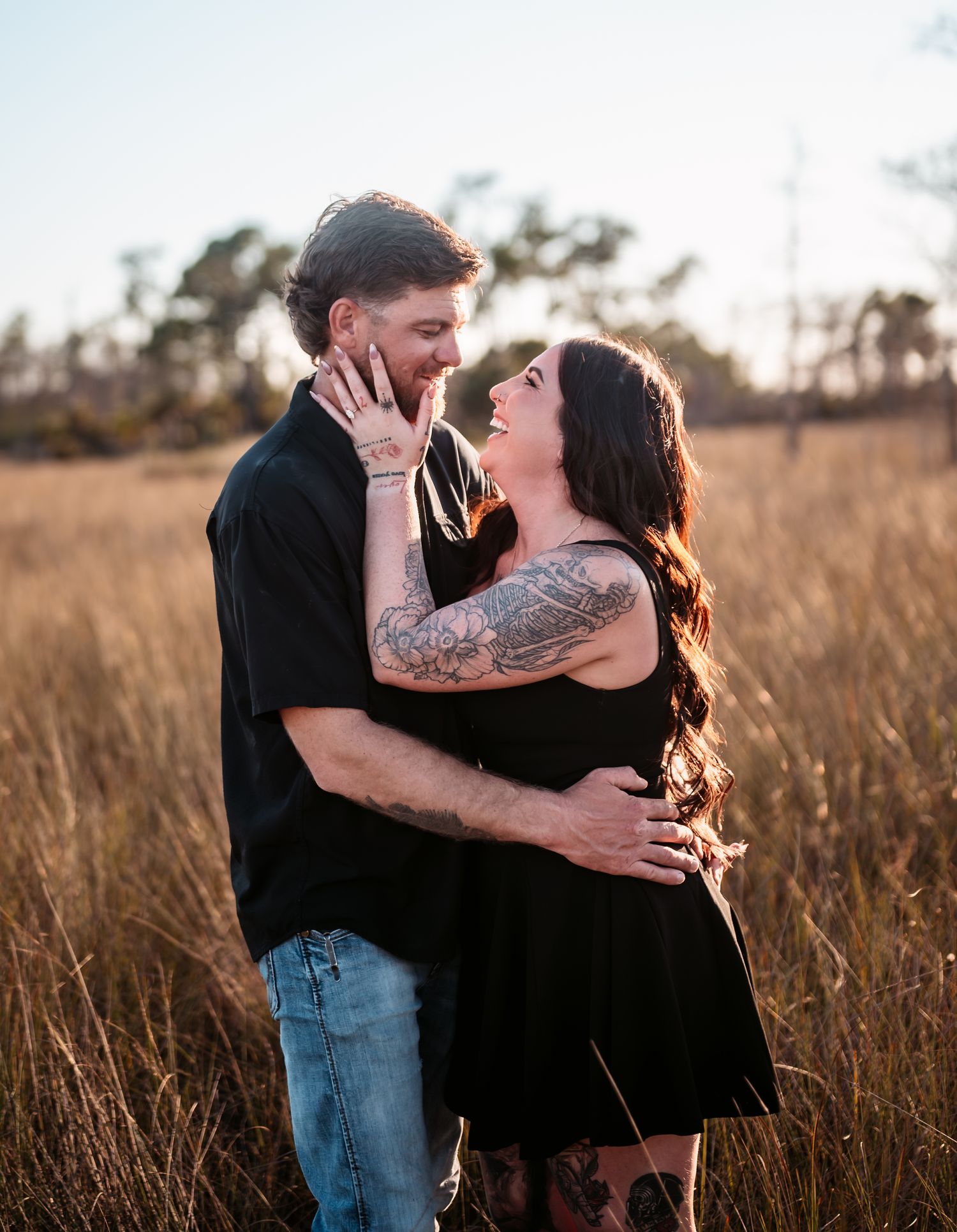 Couple shares romantic embrace in sunlit field with natural golden lighting.