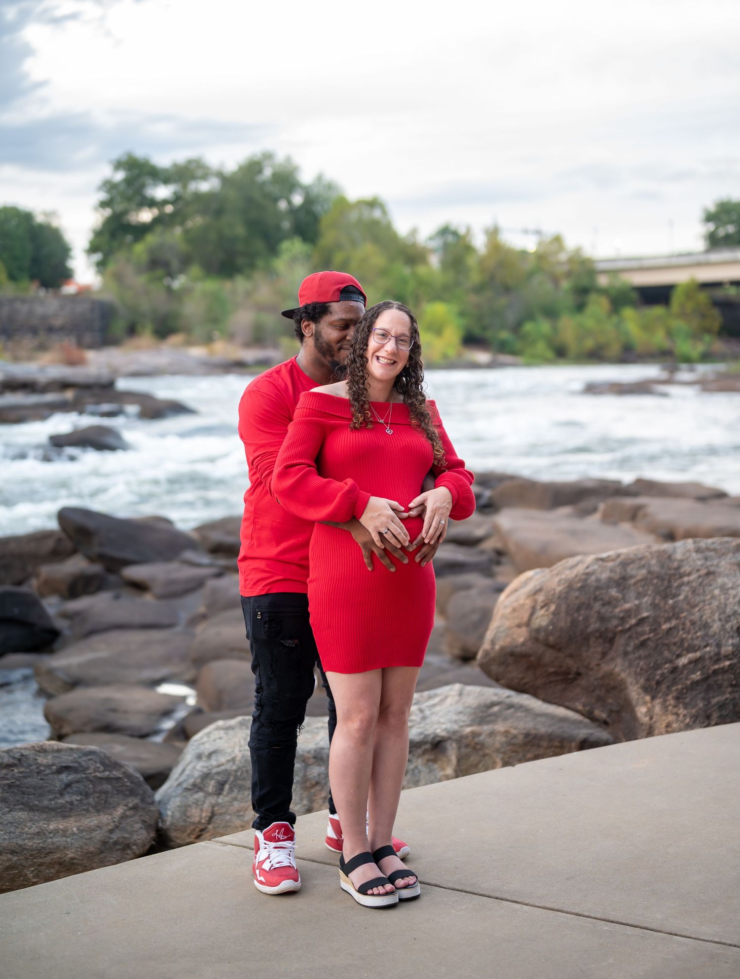 People in red outfits stand together on a rocky beach shoreline with waves and trees in the background.