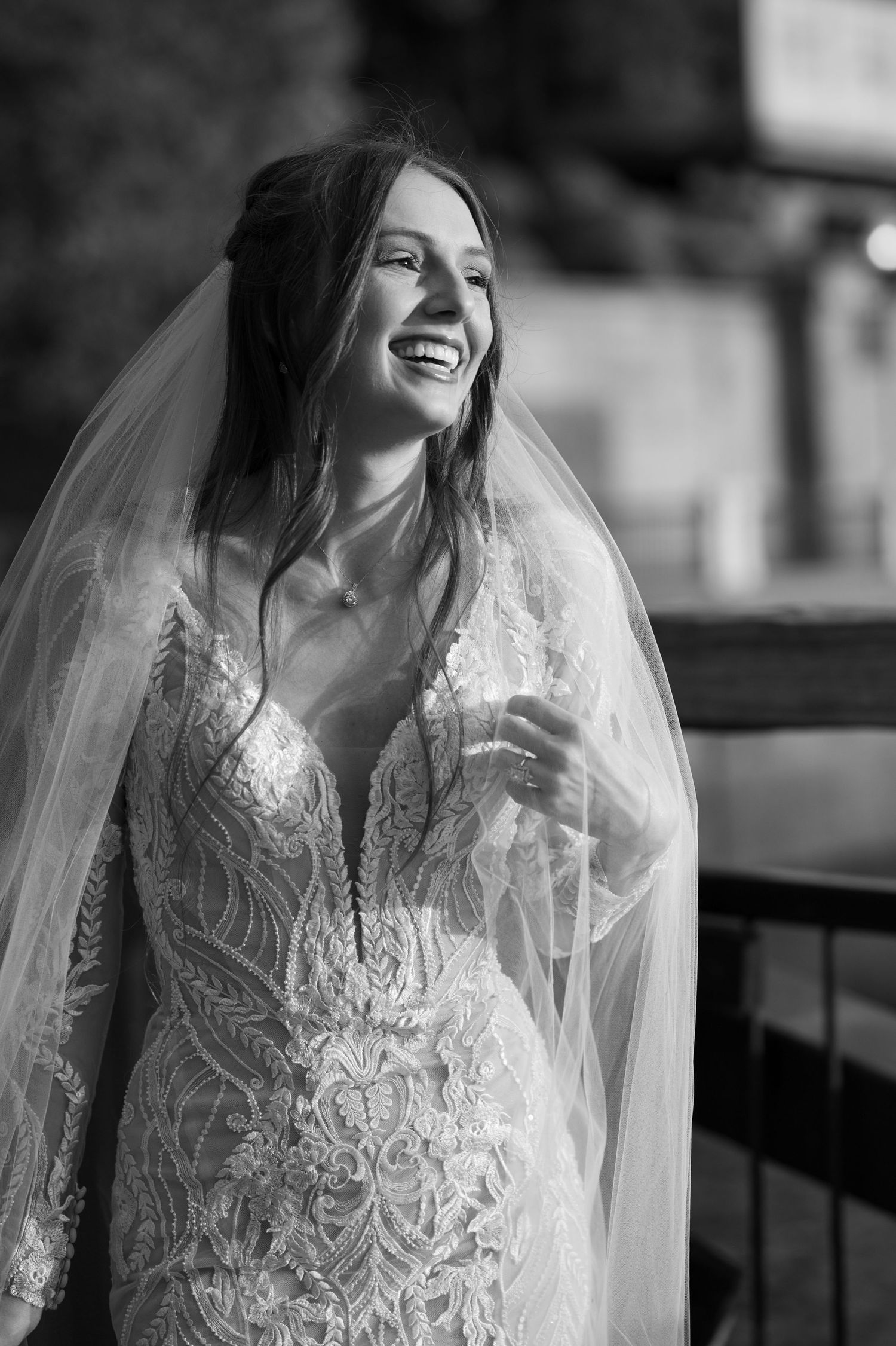Black and white portrait of a bride laughing while wearing a detailed lace gown and veil.