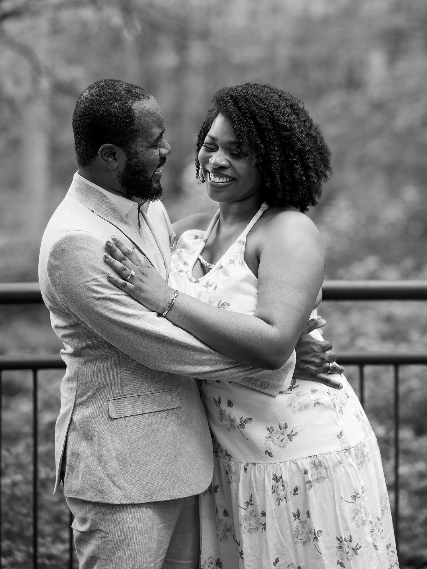 Black and white portrait of a newly engaged couple embracing and laughing together on an outdoor bridge.