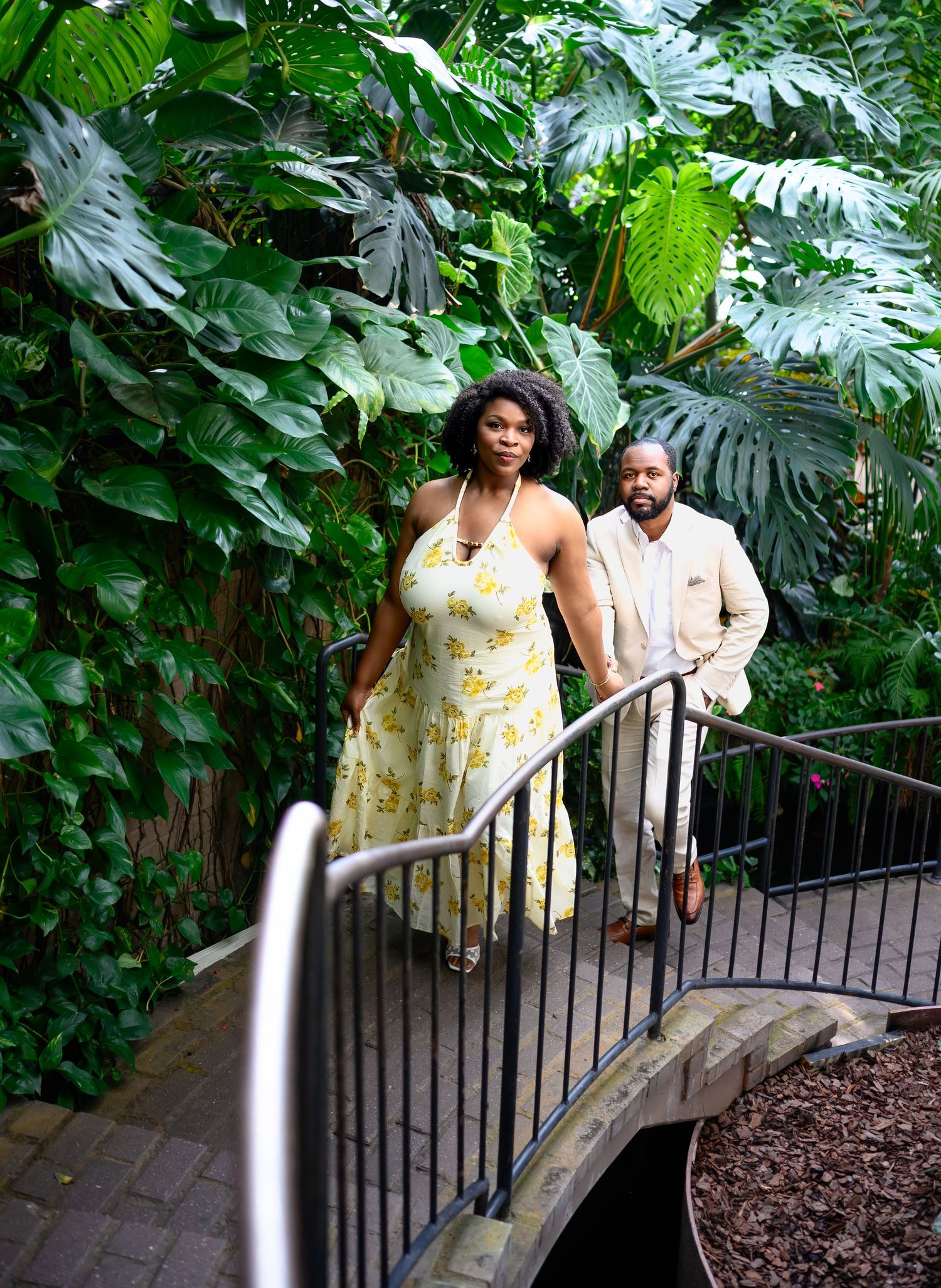 Elegant couple walking up a bridge stairway surrounded by lush tropical greenery.