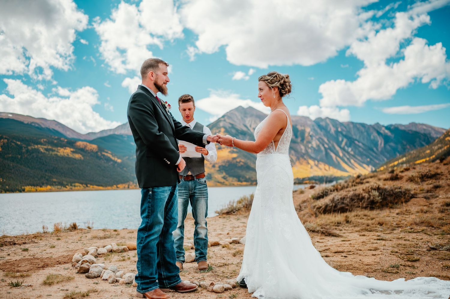 A wedding ceremony set against a beautiful mountain landscape with clouds and vibrant blue sky in Colorado.