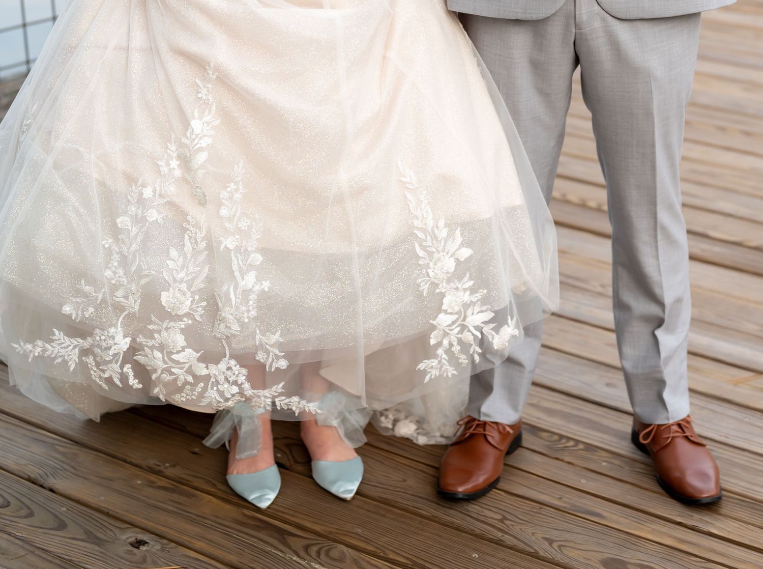 Wedding shoes and dress hem details on a rustic wooden deck.