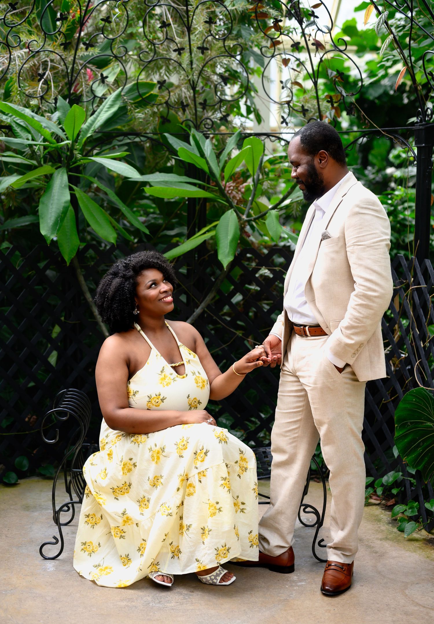 A couple shares a tender moment on a garden bench, holding hands and gazing at each other lovingly.