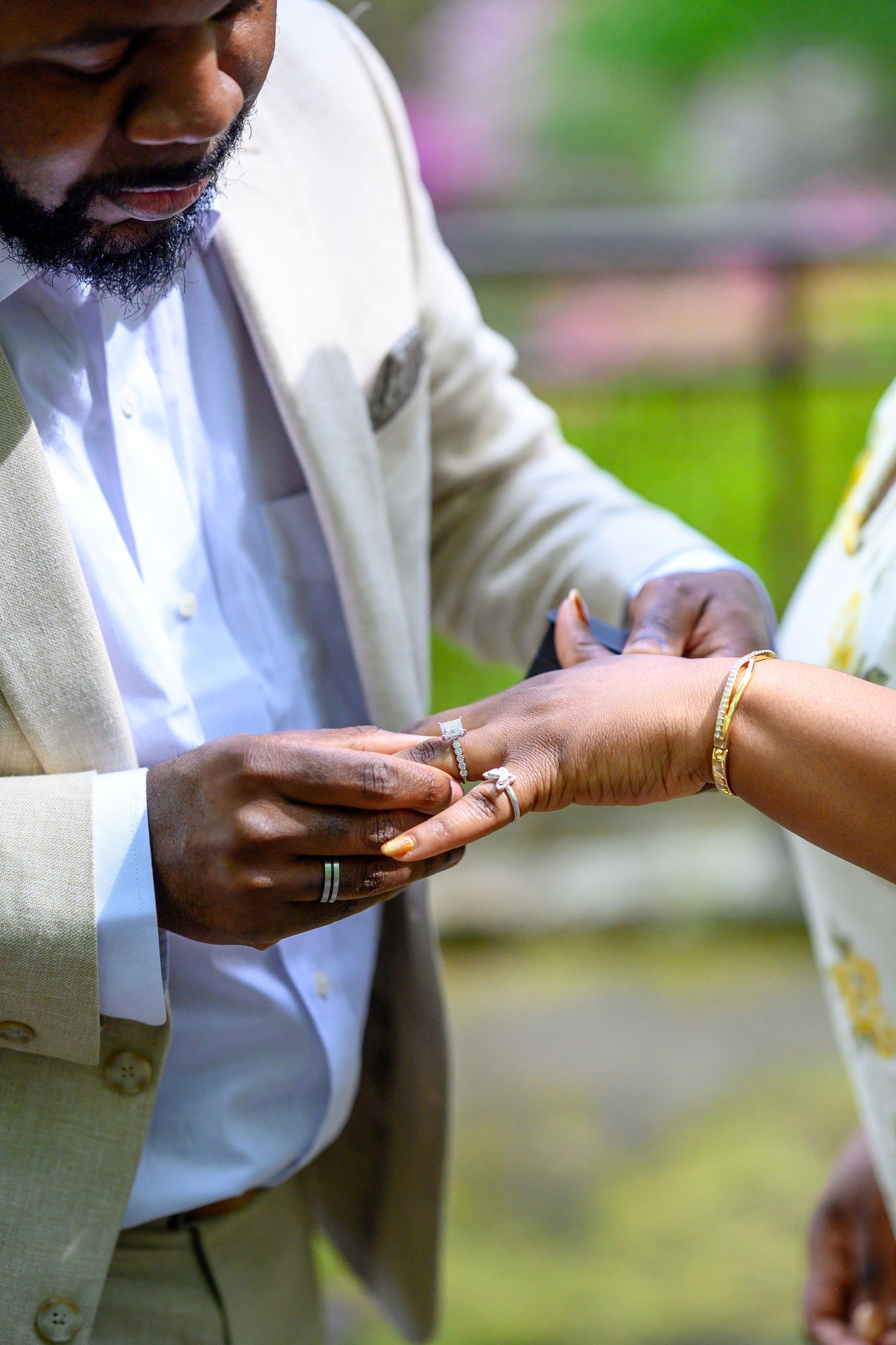 Groom placing wedding ring on bride's finger during outdoor ceremony.