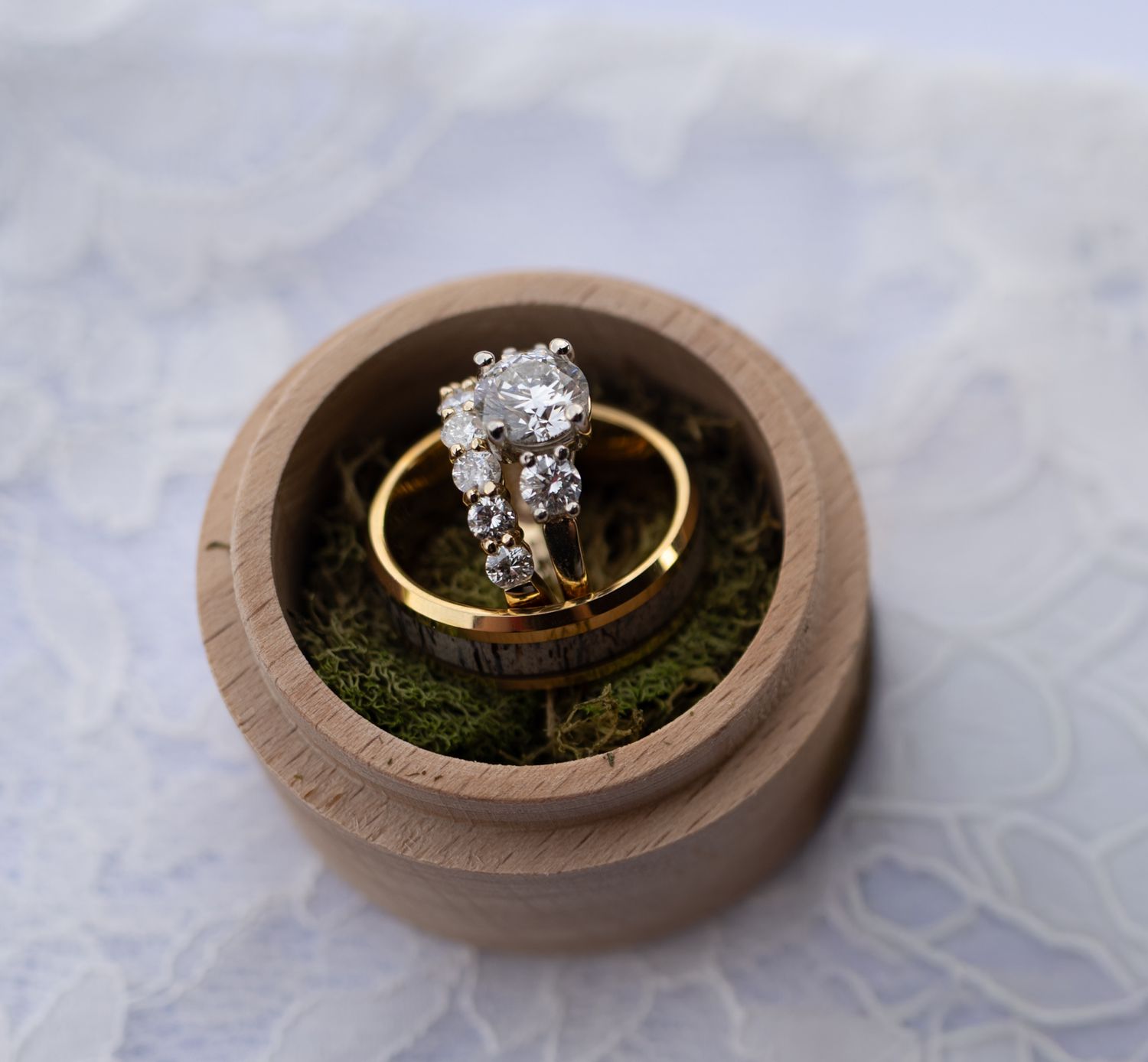 A series of images showing a gold engagement ring with diamonds displayed in a rustic wooden ring box with moss.