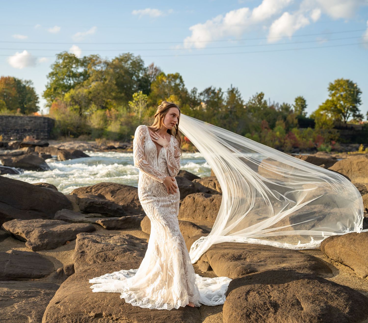 Elegant bridal portrait on rocky coastline with flowing veil catching the wind.